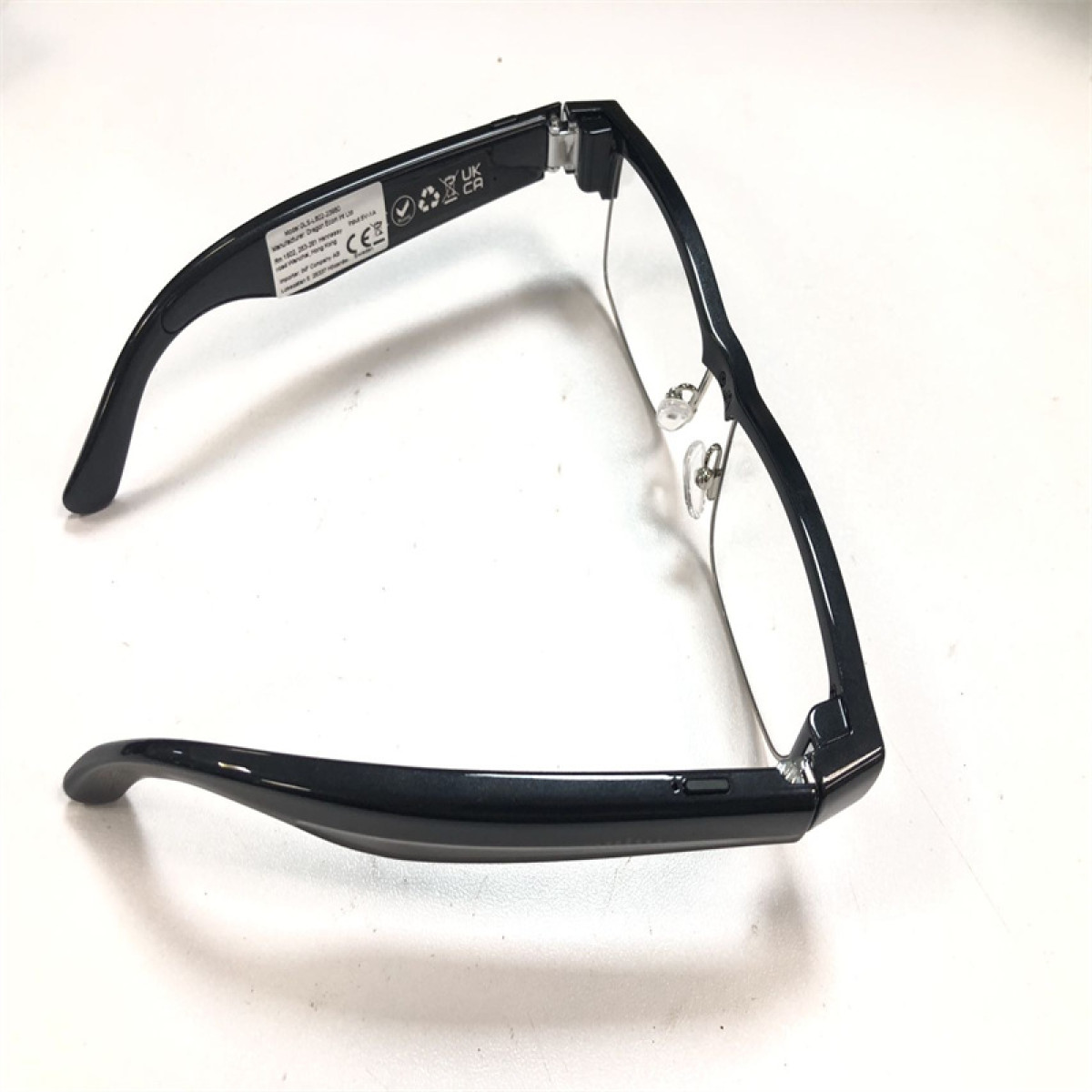 Czarne okulary z przezroczystymi soczewkami leżą na białej powierzchni, rzucając cień.