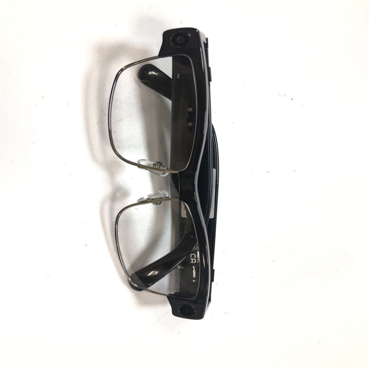 Czarna oprawka okularów z przezroczystymi soczewkami spoczywa na białej powierzchni.