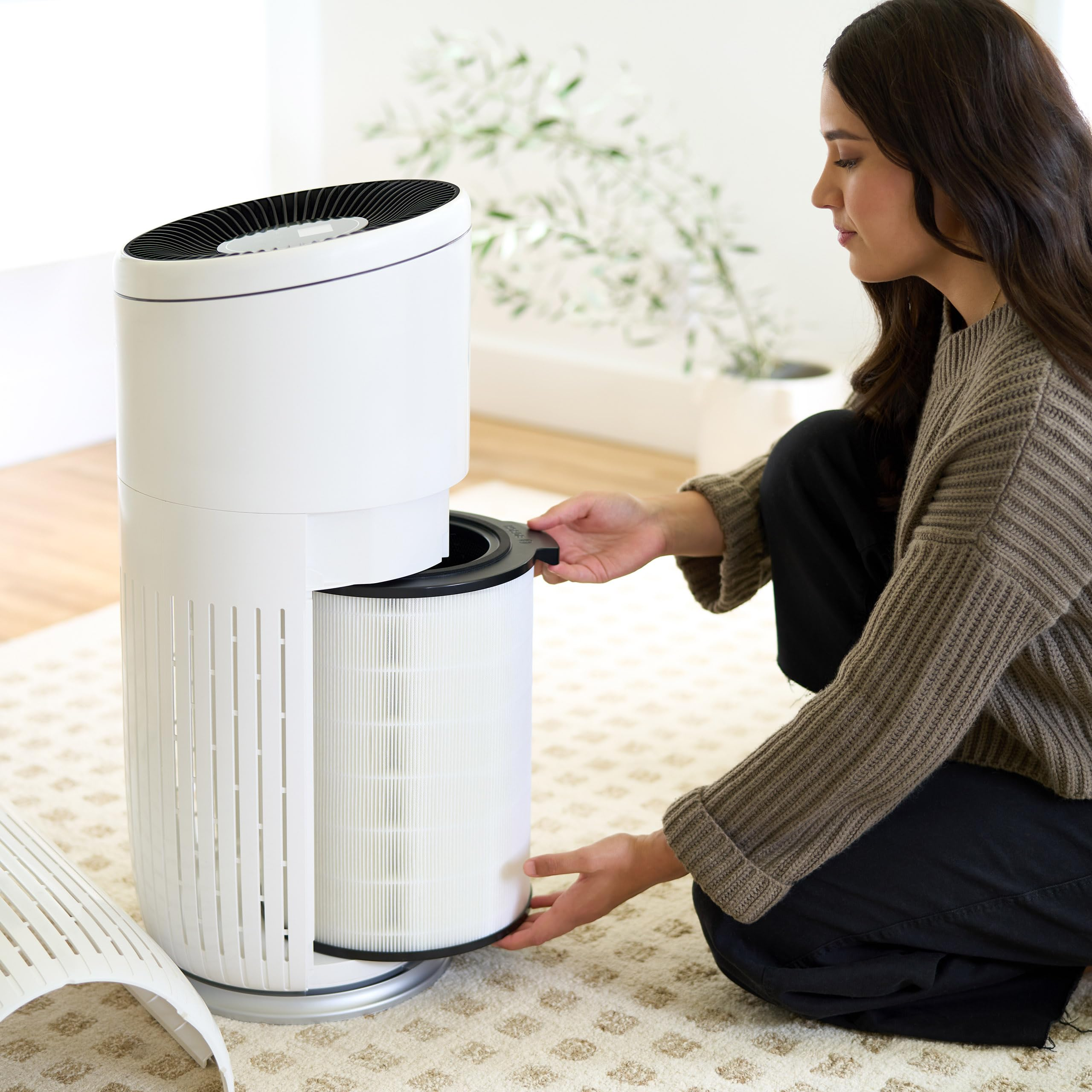 Una donna cambia un filtro dell'aria in un purificatore d'aria bianco in un soggiorno.