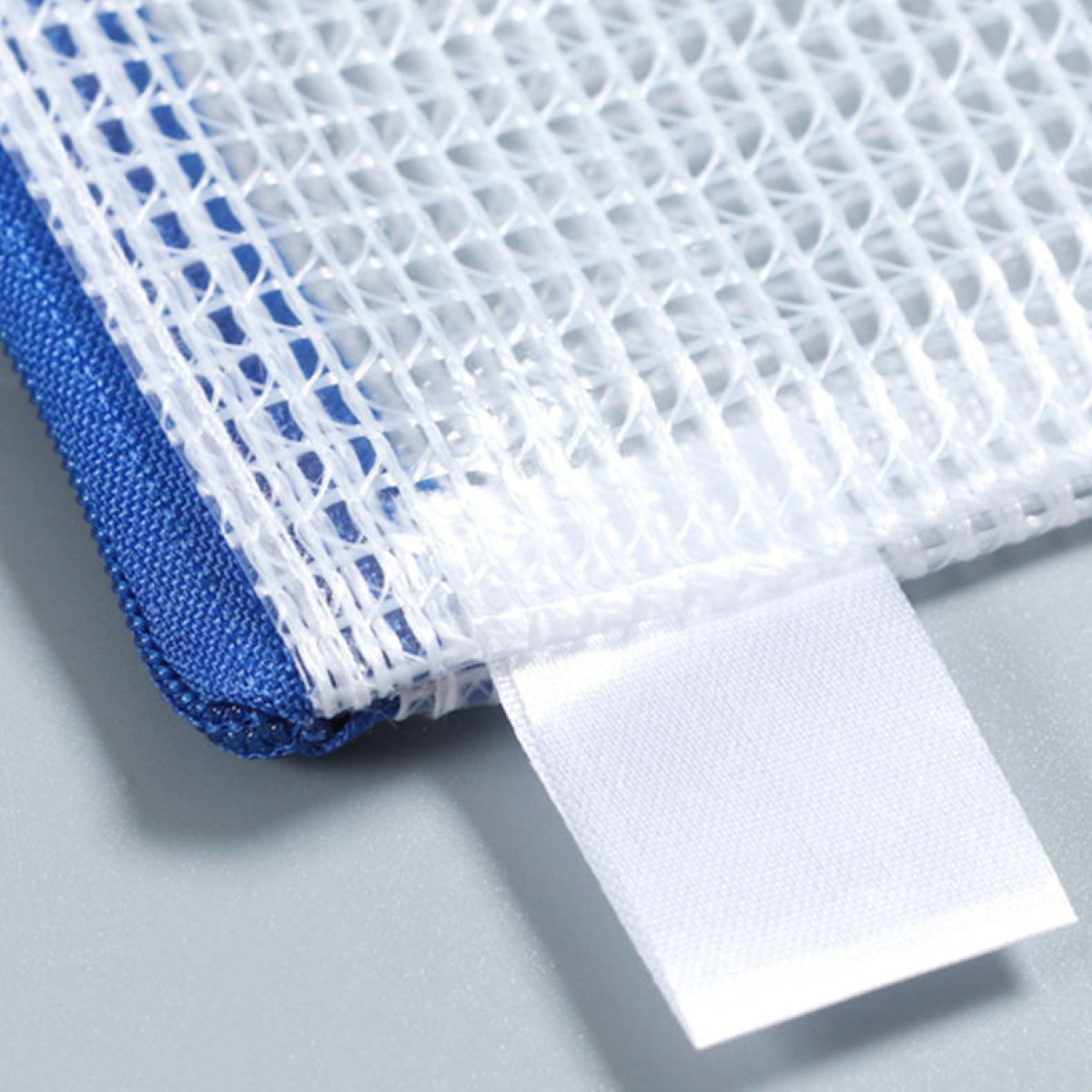 Zbliżenie białej siatkowej torby na pranie z niebieską krawędzią materiału i białą metką.