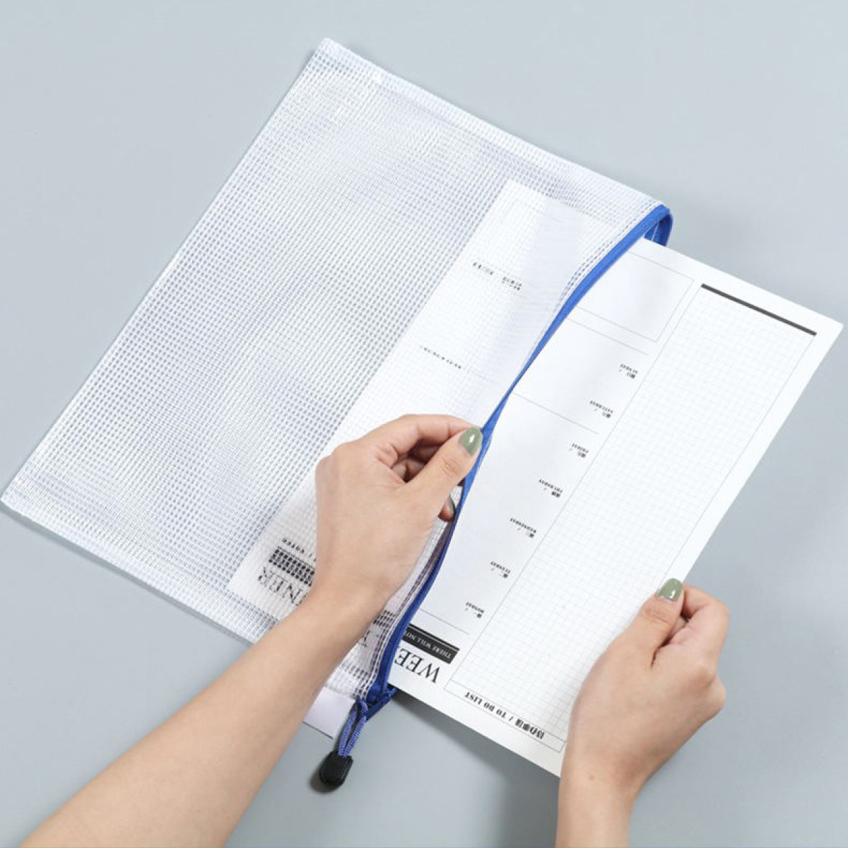 Ręce otwierają białą siatkową torbę z niebieskim zamkiem, w środku arkusz tygodniowego planu.