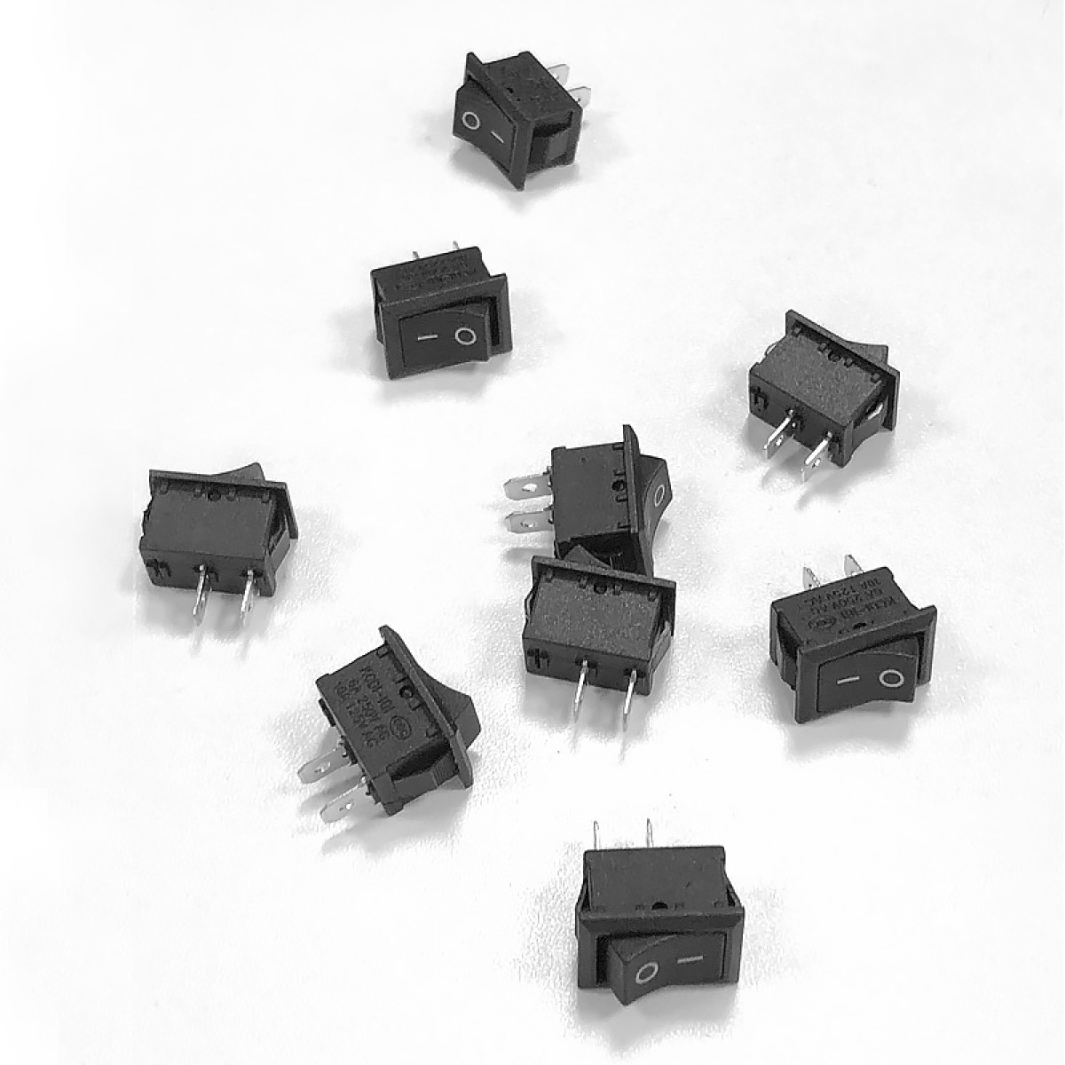 Kilka czarnych prostokątnych przełączników kołyskowych z metalowymi pinami na białej powierzchni.