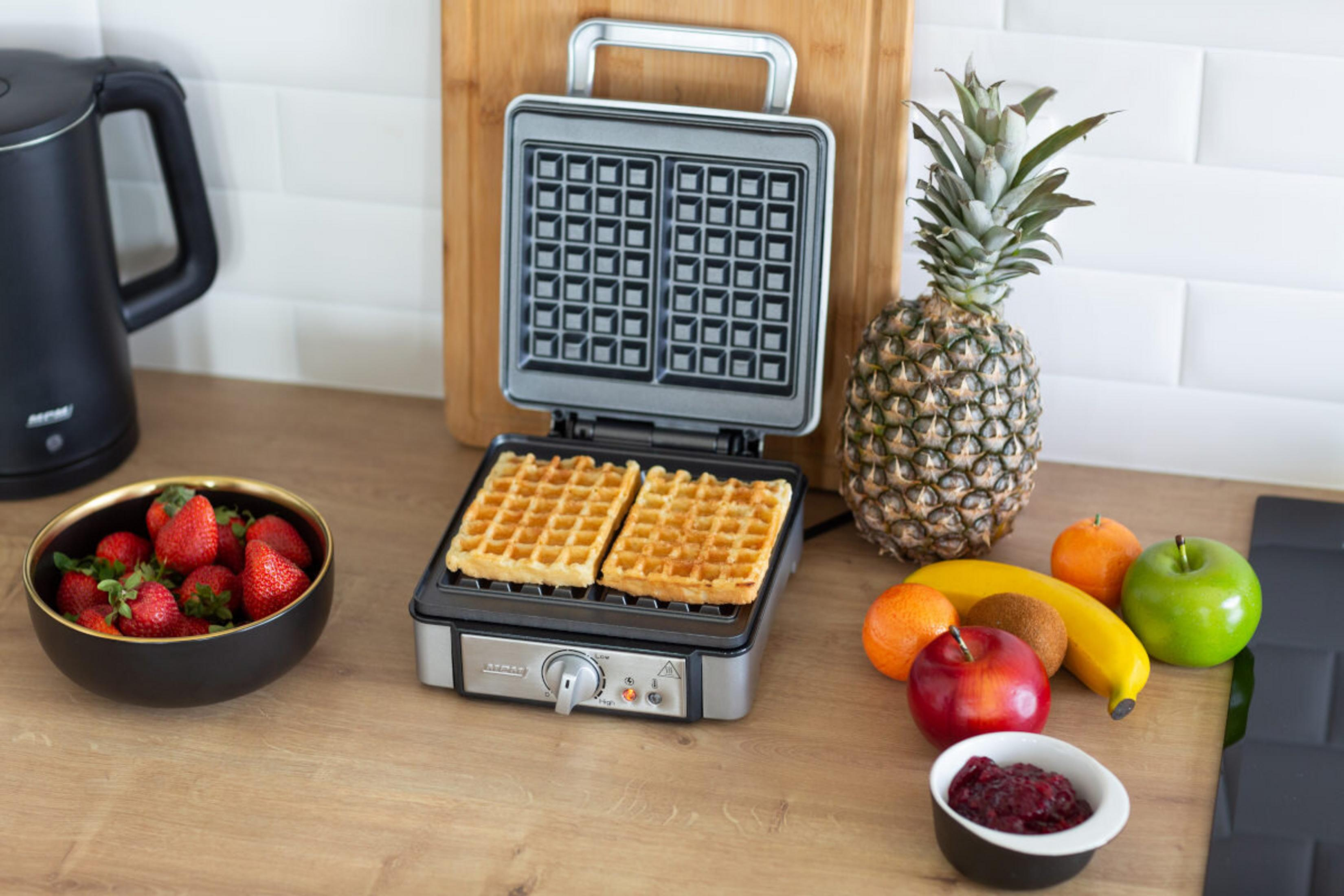 Ein Waffeleisen mit zwei Waffeln, Obst und einer Schale Erdbeeren.