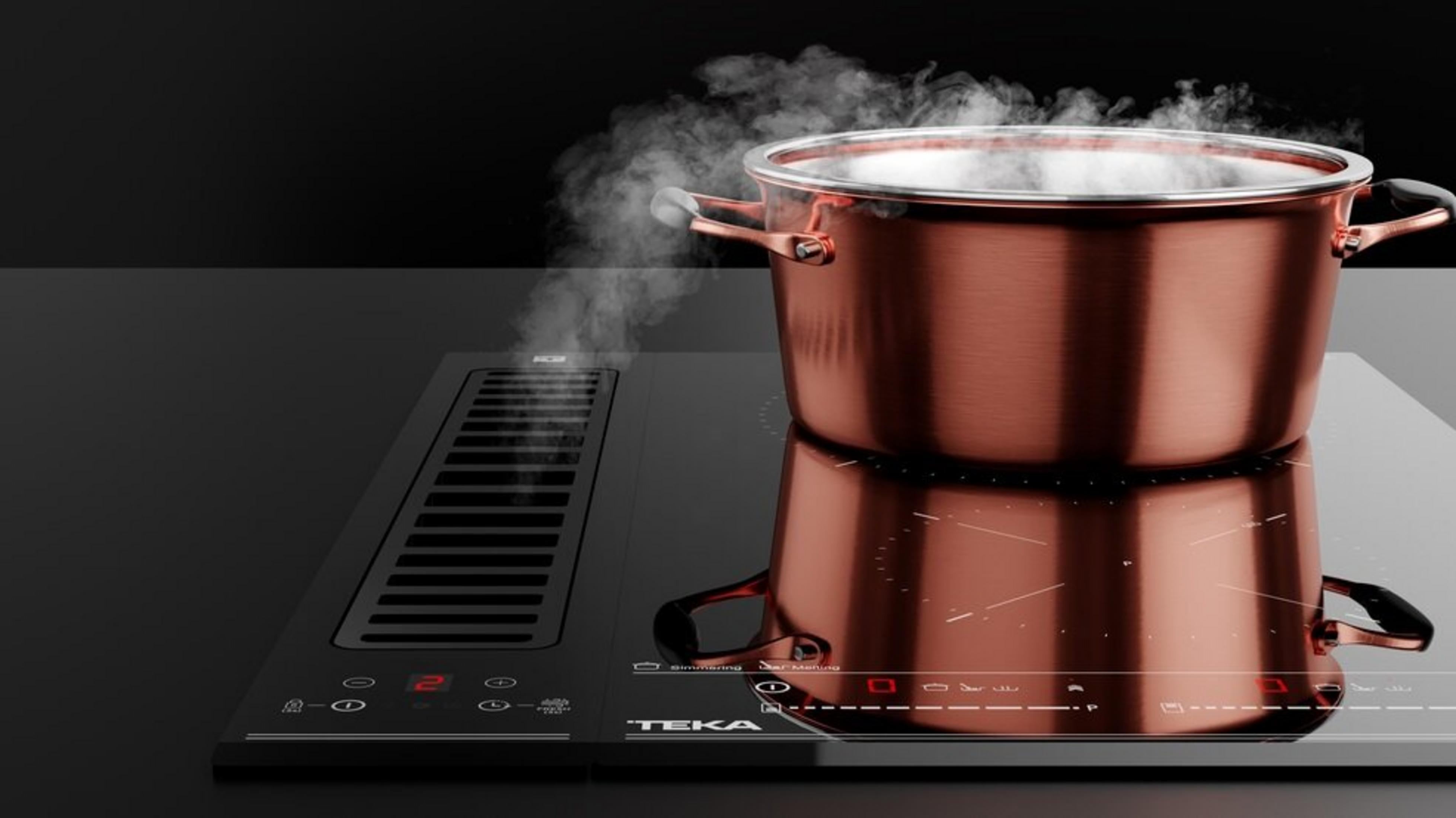 Una olla de cobre humea en una placa de inducción negra con ventilación.
