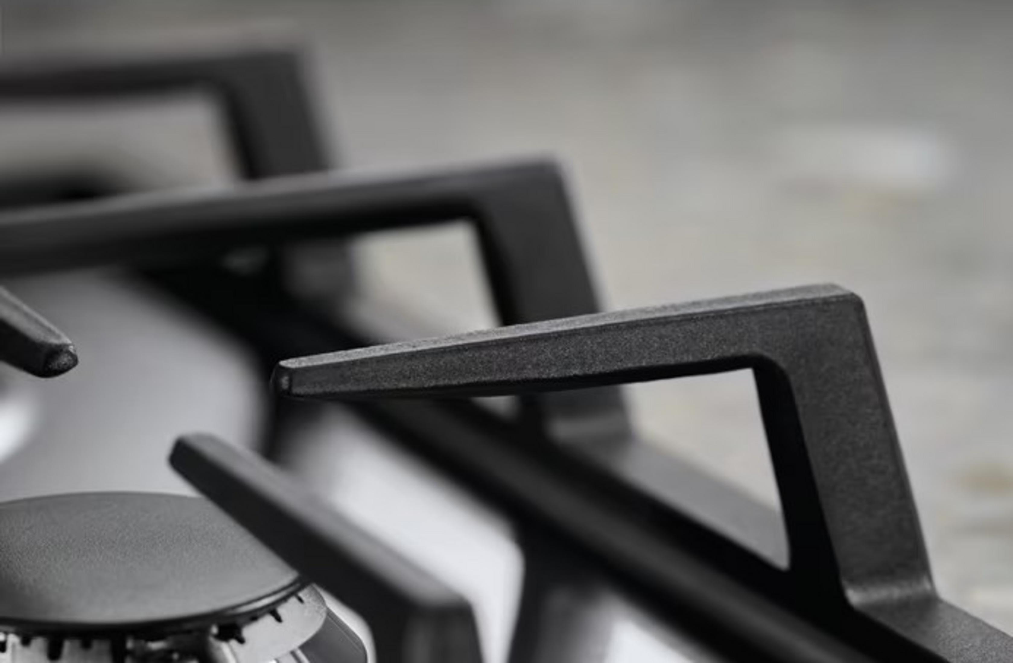 Zbliżenie czarnych rusztów kuchenki gazowej na srebrnej kuchence. Szare tło.