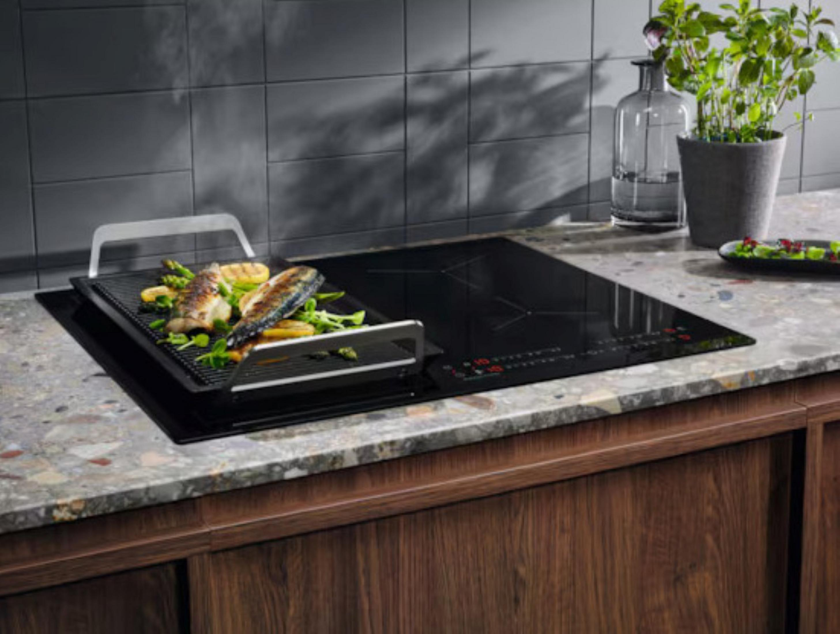 Un piano cottura a induzione moderno con accessorio grill che cuoce pesce e asparagi.