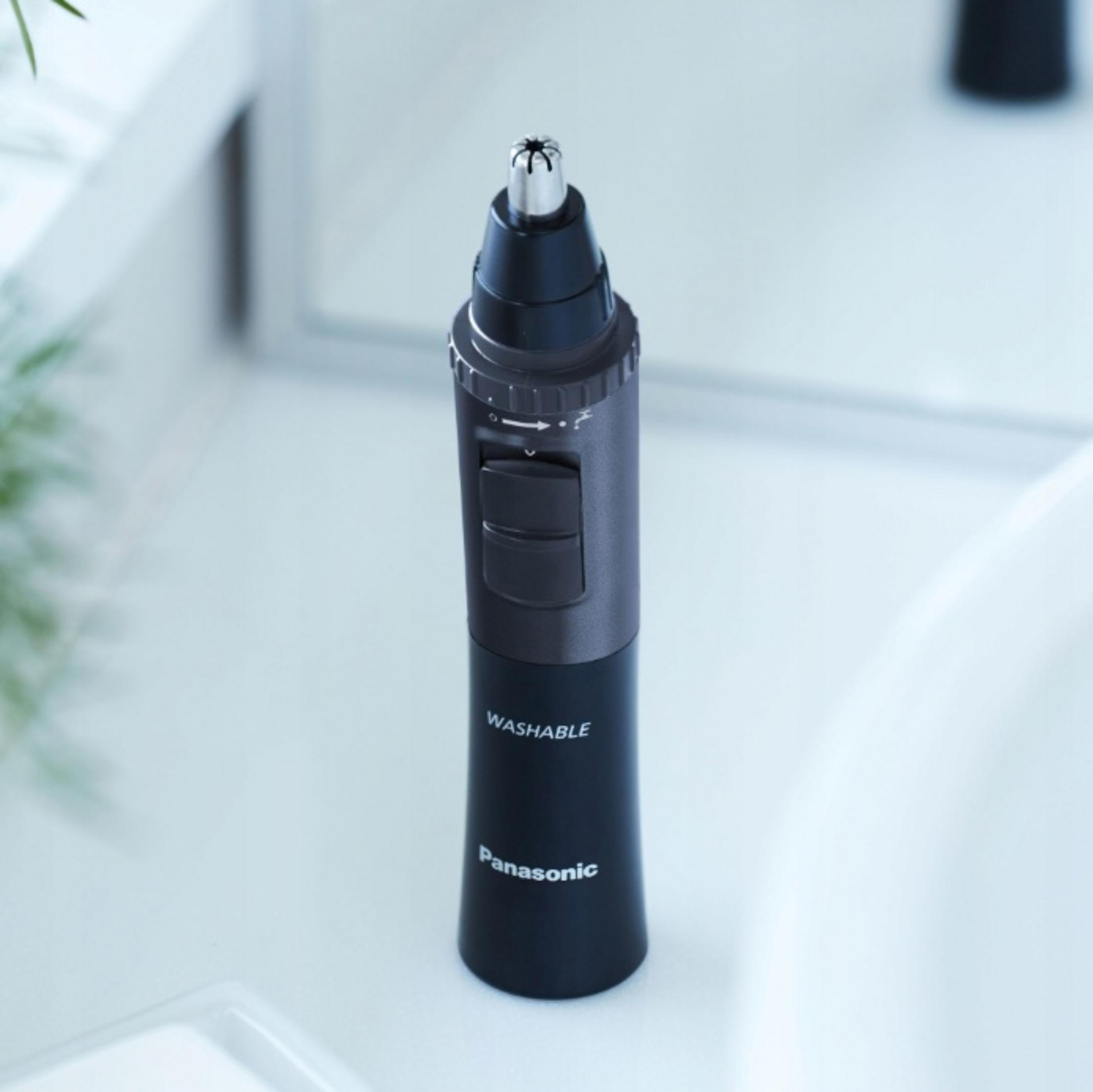 Un recortador de vello nasal Panasonic negro con punta plateada sobre superficie blanca.