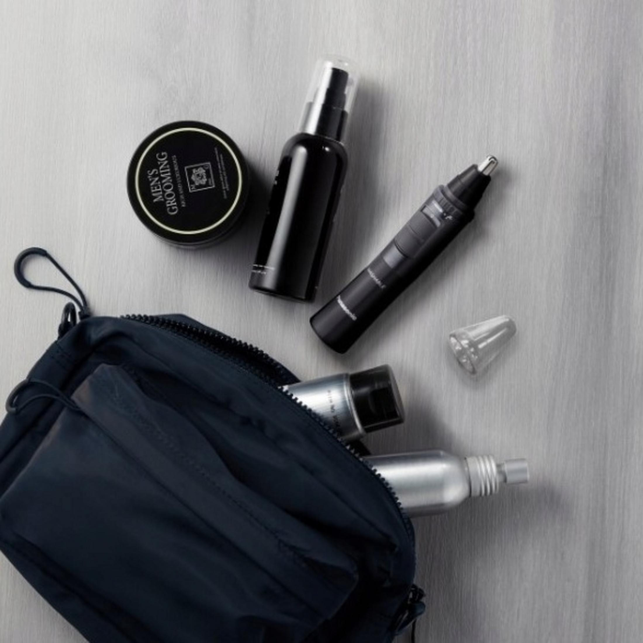 Productos de aseo masculino: tarro, botella, recortadora y spray en bolsa azul marino.