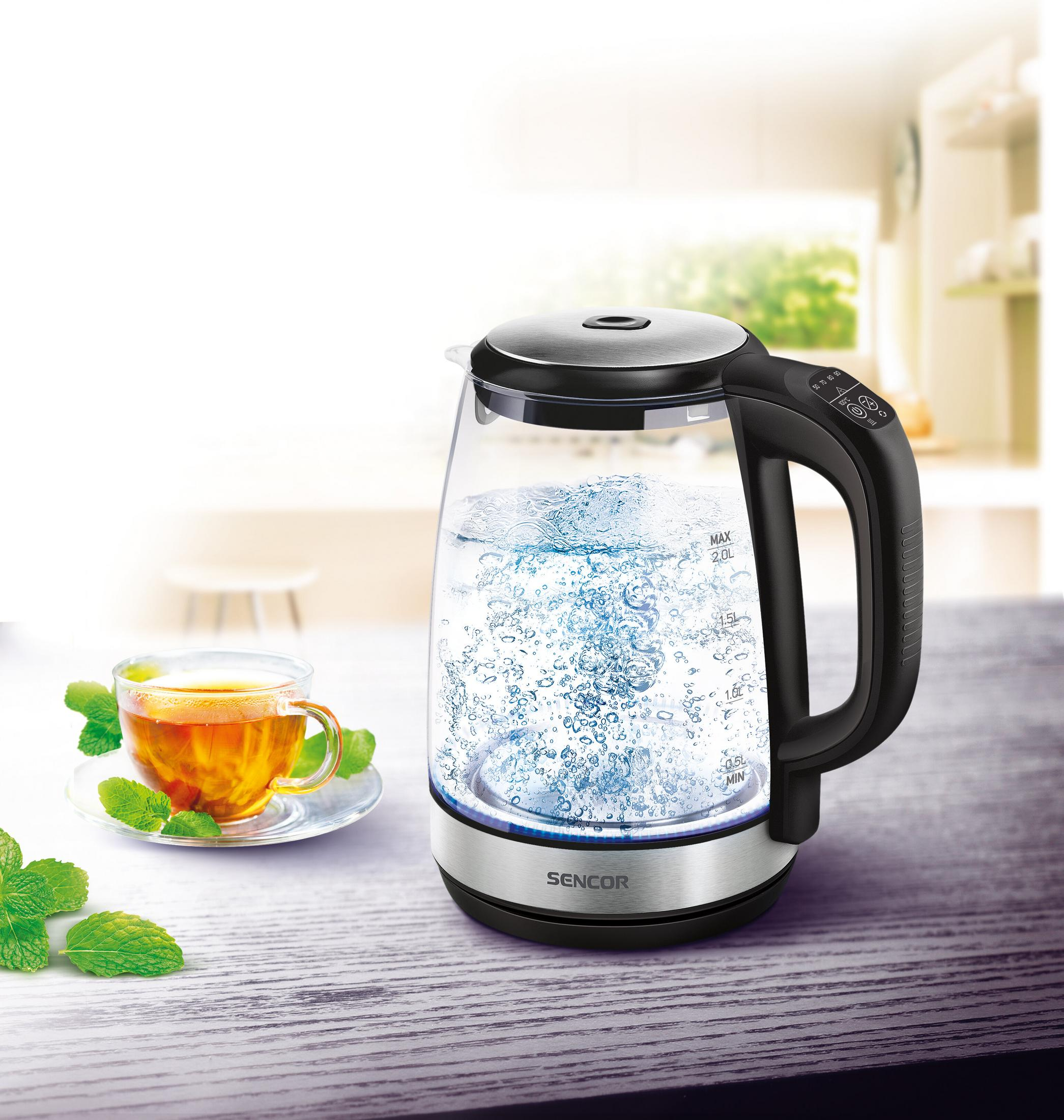 Ein Sencor-Wasserkocher aus Glas mit kochendem Wasser und eine Tasse Tee mit Minzblättern.