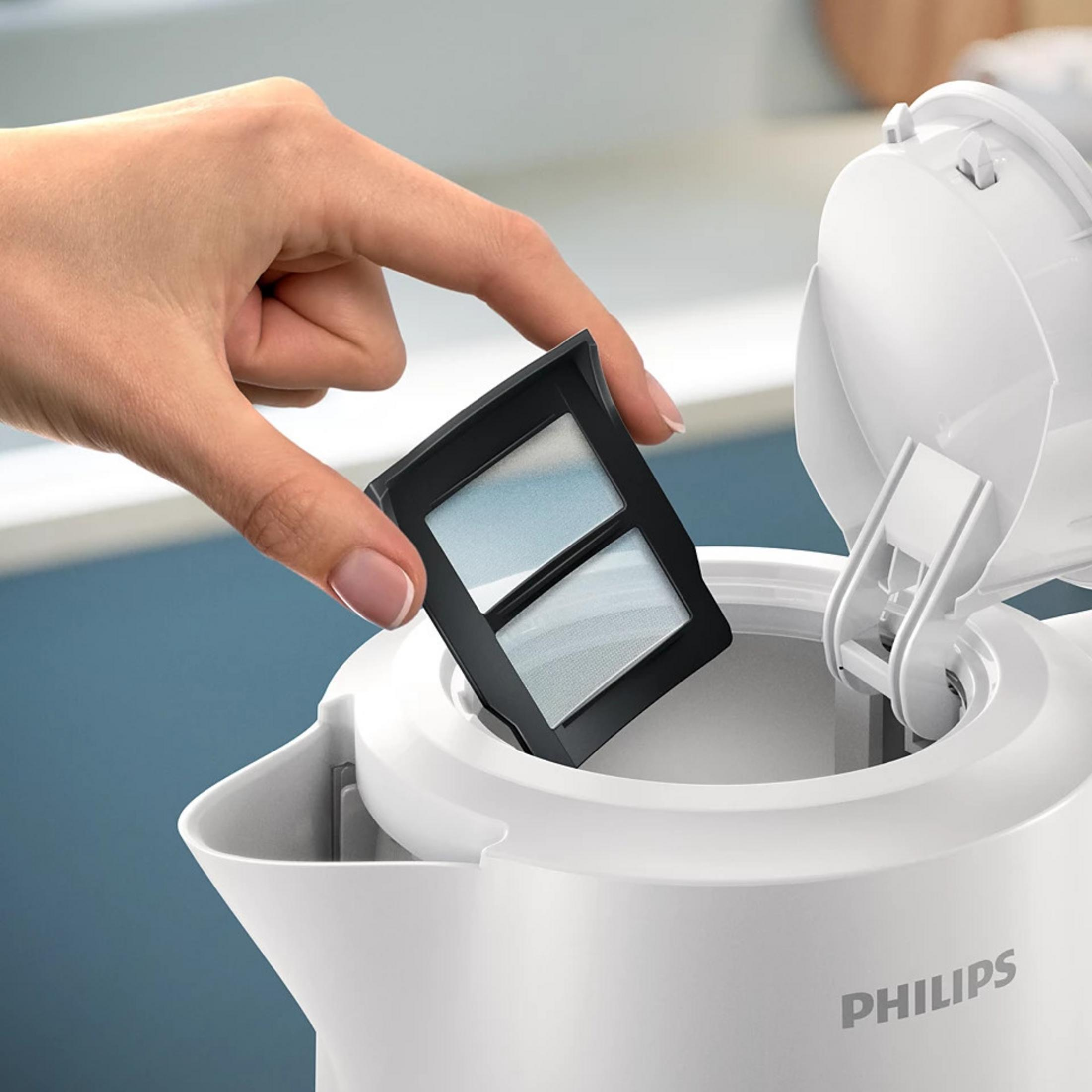 A hand holds a black filter over a white electric kettle.