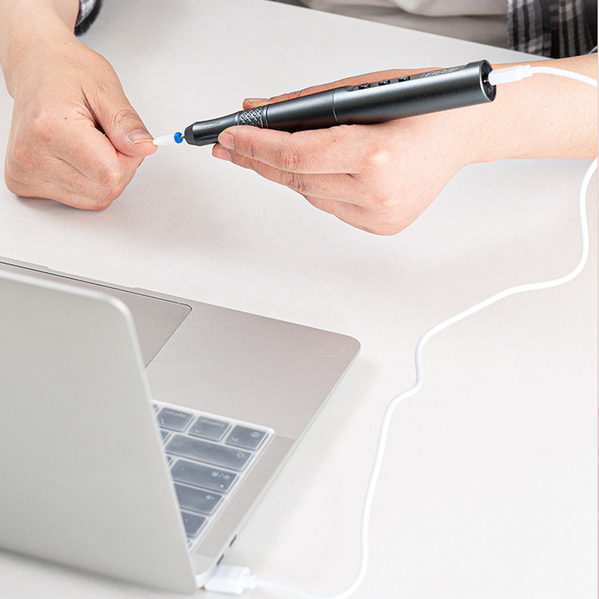 Eine Person schließt ein USB-Kabel von einem grauen stiftähnlichen Gerät an einen Laptop an.
