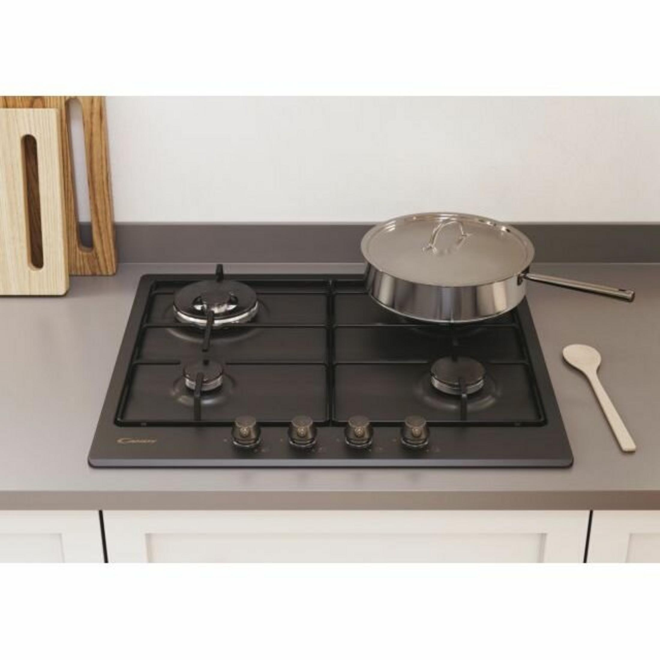 Czarna płyta gazowa z garnkiem pod przykryciem i drewnianą łyżką.