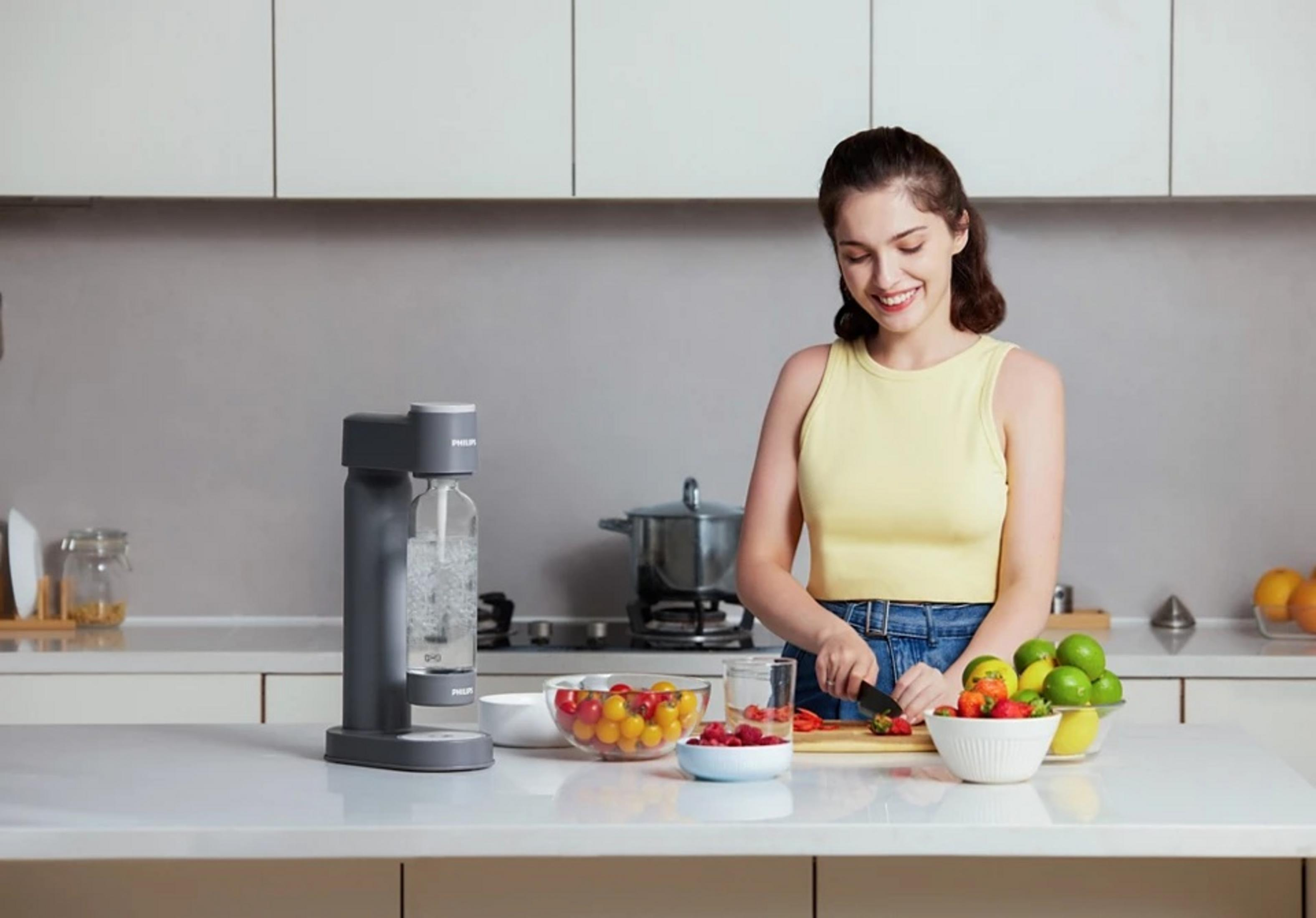 Una donna taglia frutta in una cucina accanto a una macchina per soda e ciotole di frutta.