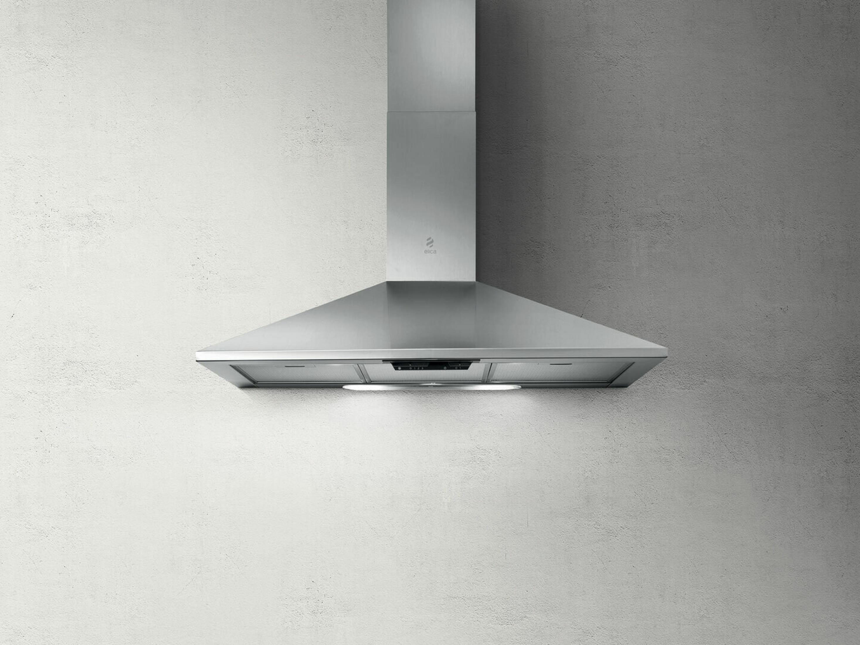 Cappa in acciaio inox con comandi touch e luce su parete testurizzata.