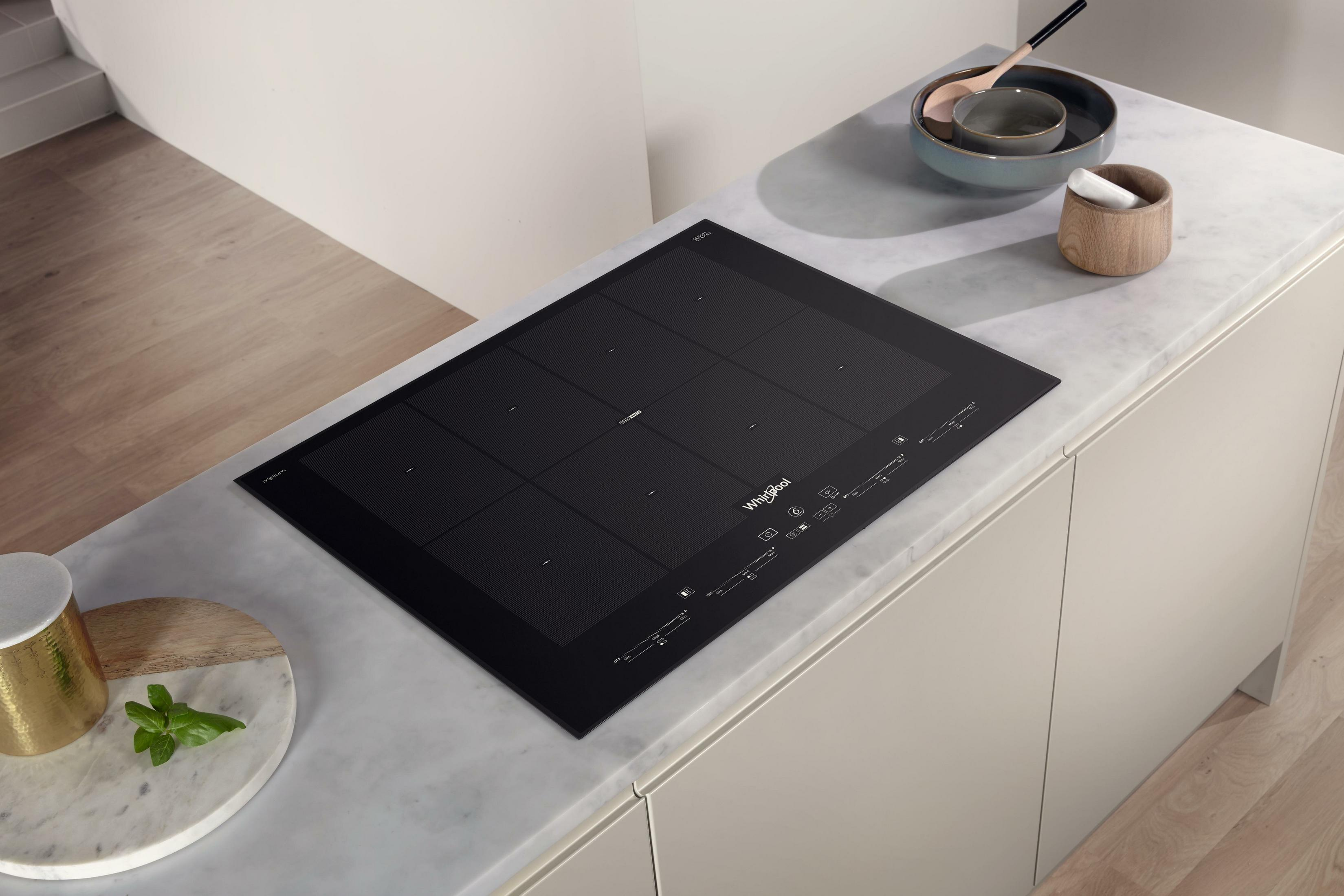 Una placa de inducción Whirlpool negra está sobre una encimera de mármol, con utensilios de cocina cerca.
