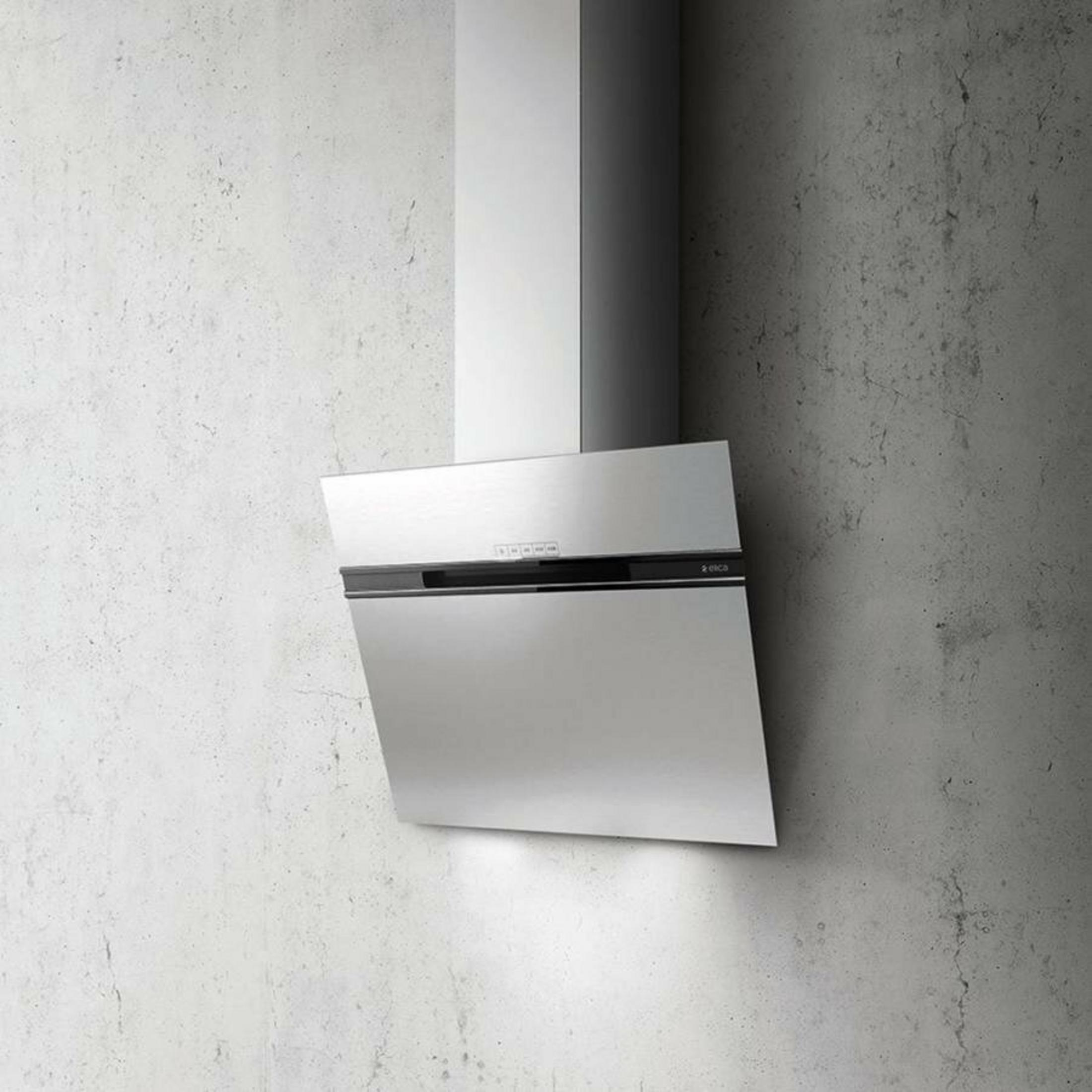 Cappa in acciaio inox davanti a un muro di cemento con luci.