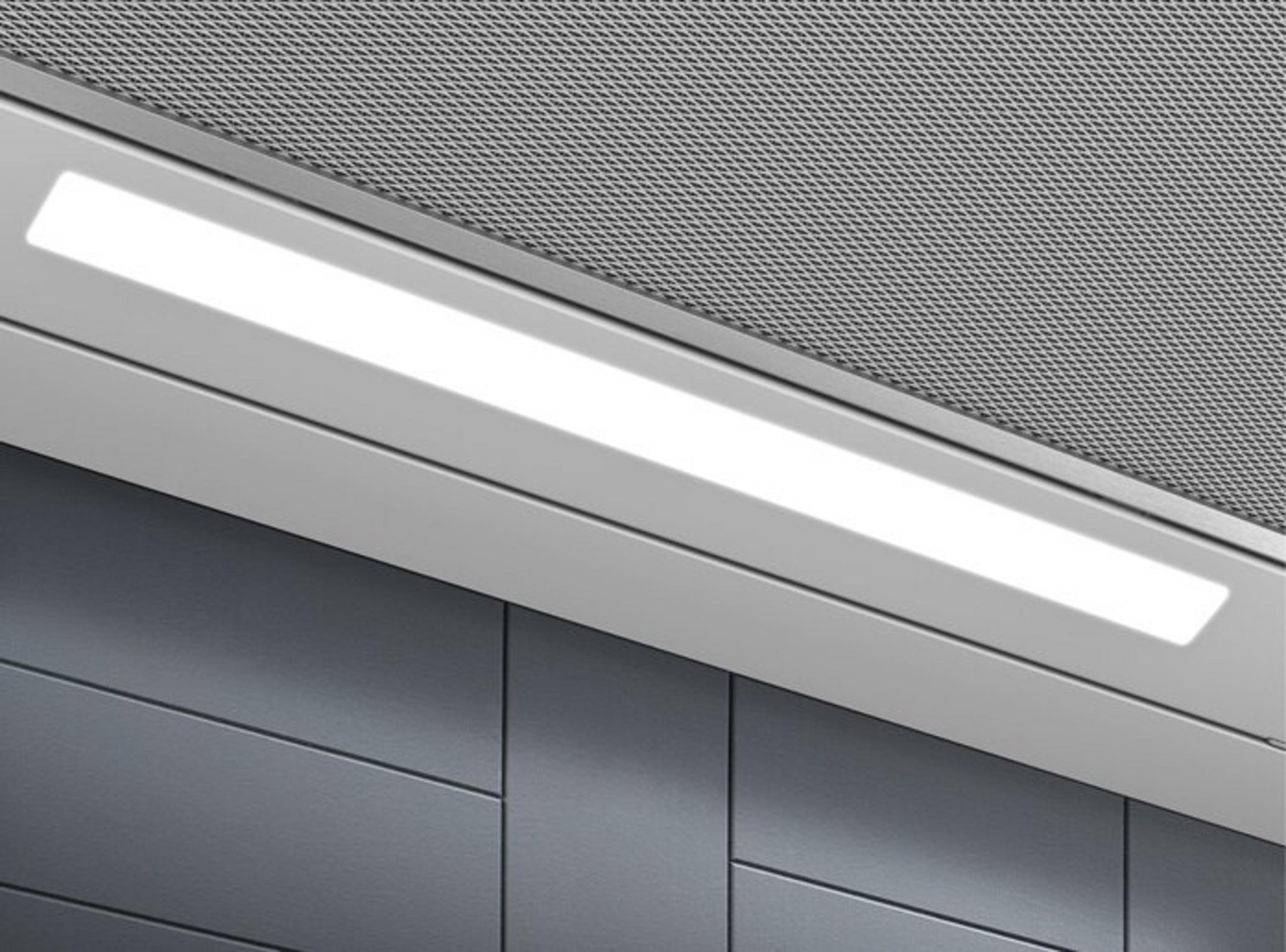 Una barra luminosa a LED luminosa sopra pannelli grigio scuro sotto una grata metallica perforata.