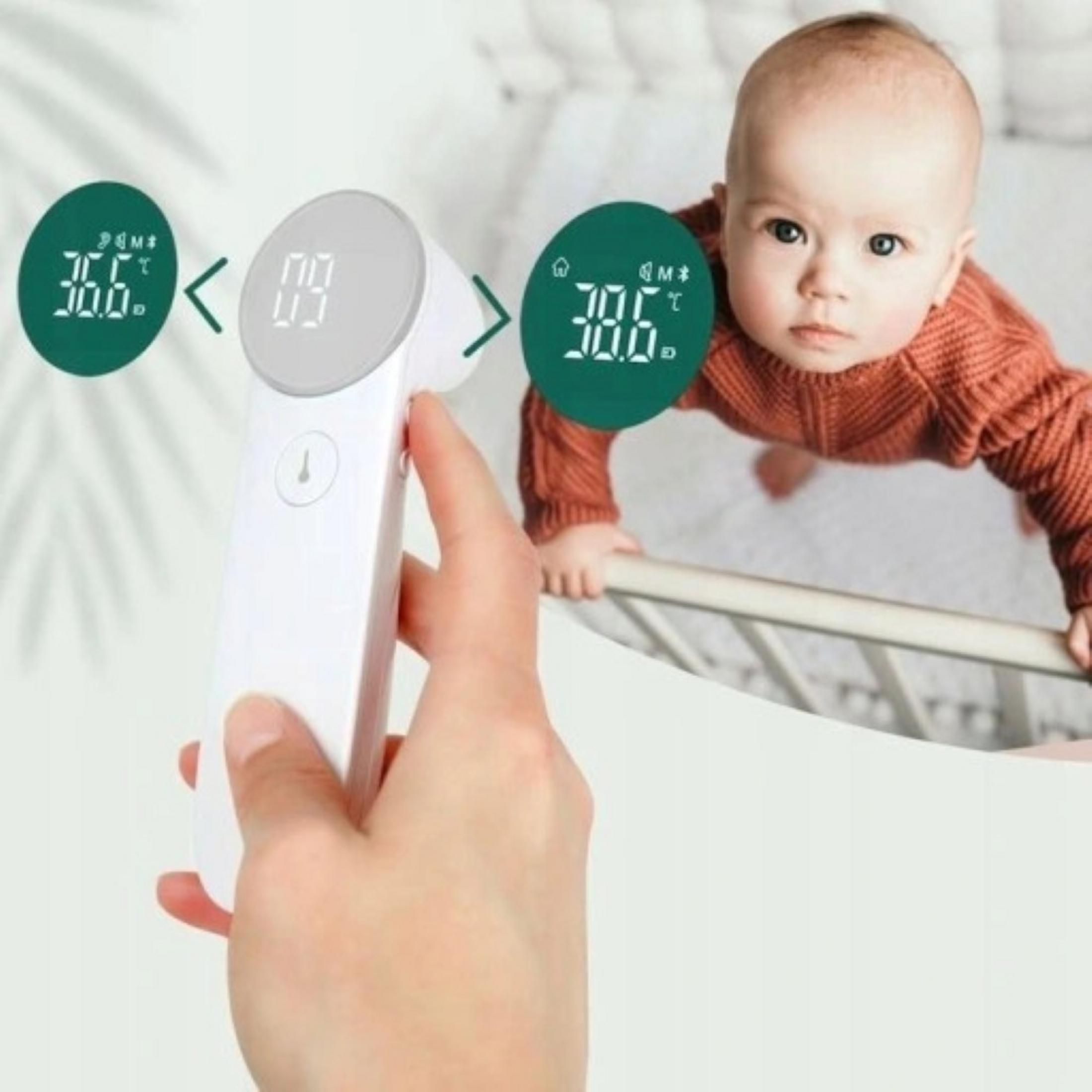 Dziecko w koralowym sweterku leży w łóżeczku, ręka trzyma termometr. Wyświetlacz cyfrowy 36.6C.