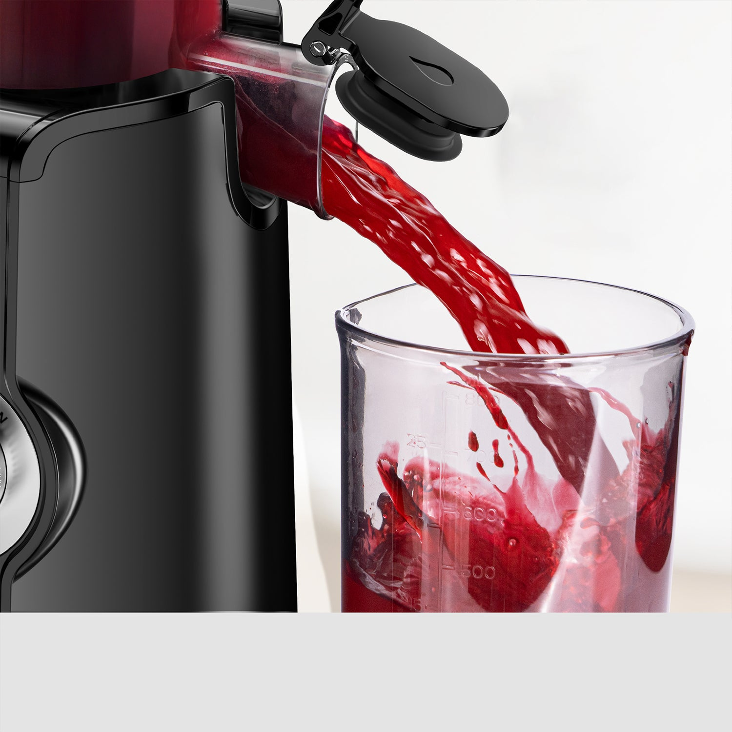 Un estrattore nero eroga succo rosso in un misurino trasparente.