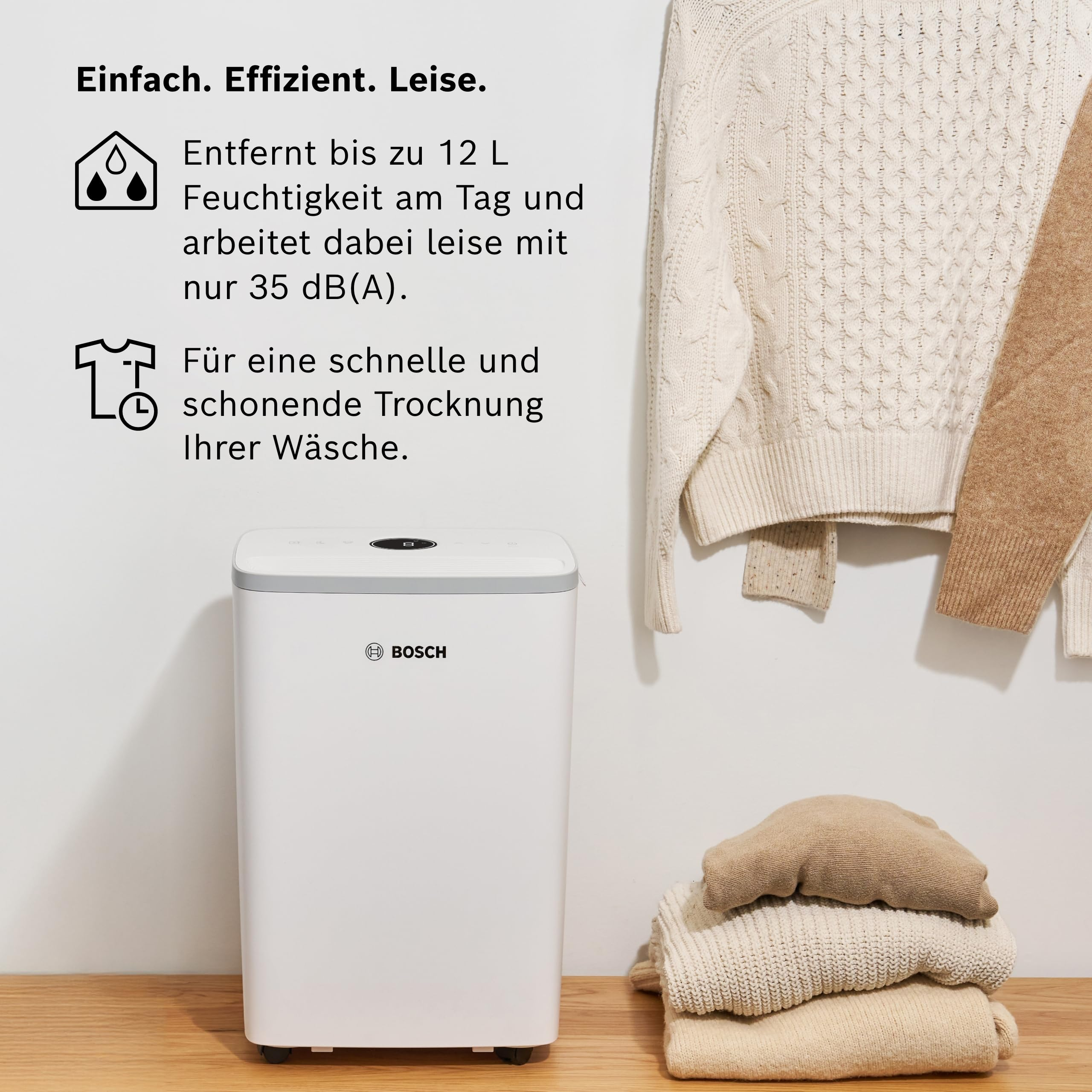 Un deumidificatore Bosch bianco accanto a maglioni piegati e appesi.