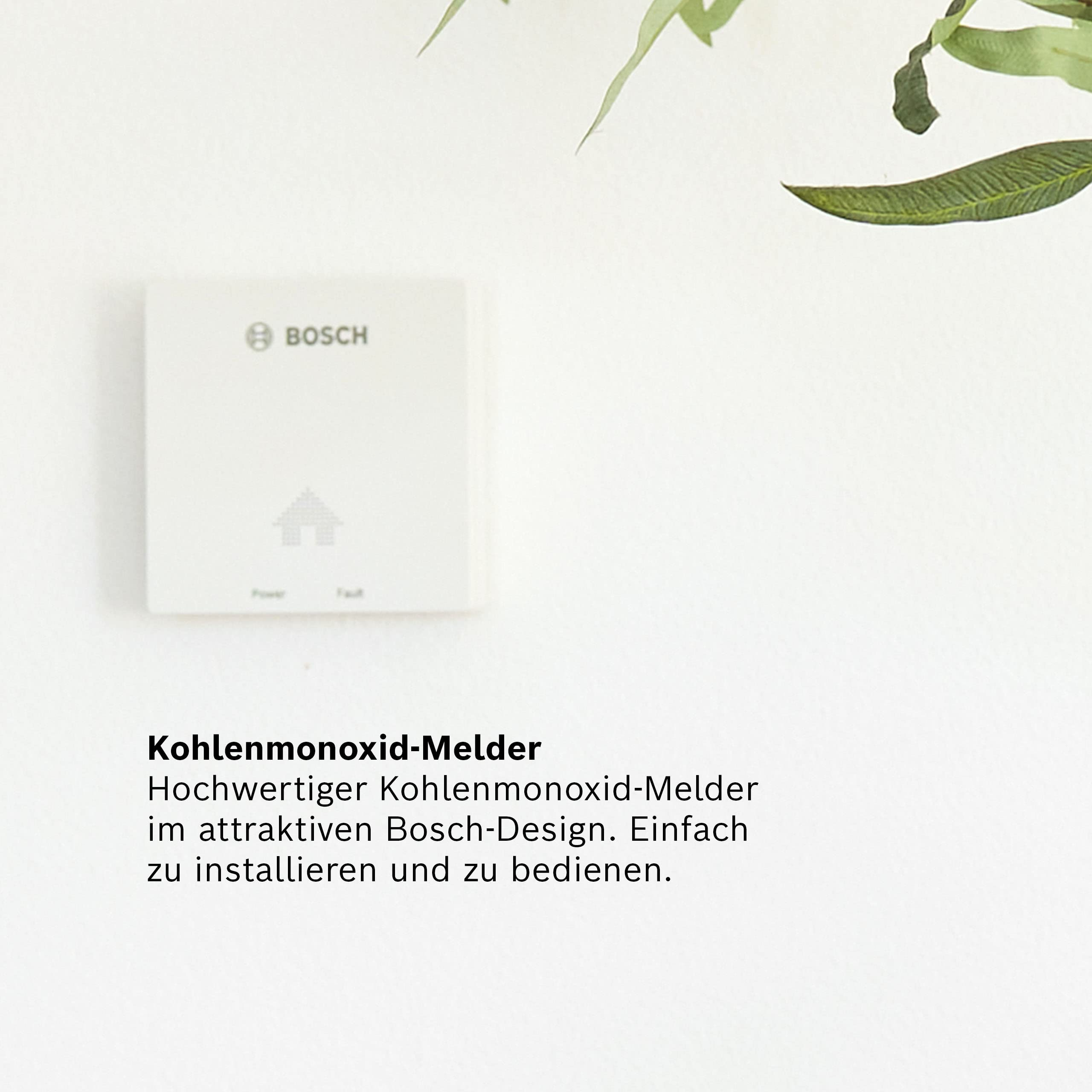 Ein weißer Bosch-Kohlenmonoxidmelder ist an einer weißen Wand montiert. Oben rechts sind grüne Blätter.