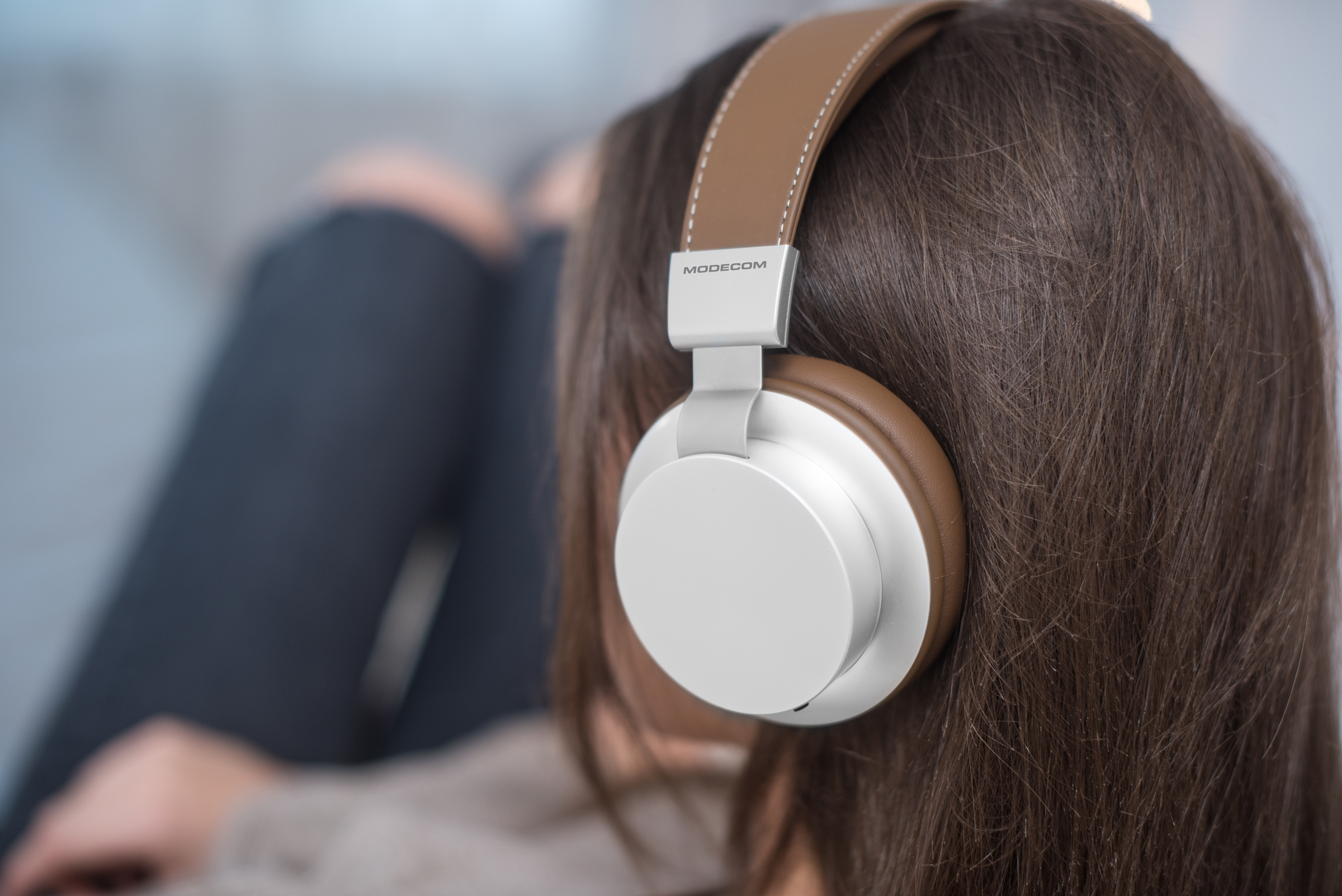 Zbliżenie osoby noszącej białe i brązowe słuchawki na ciemnobrązowych włosach.