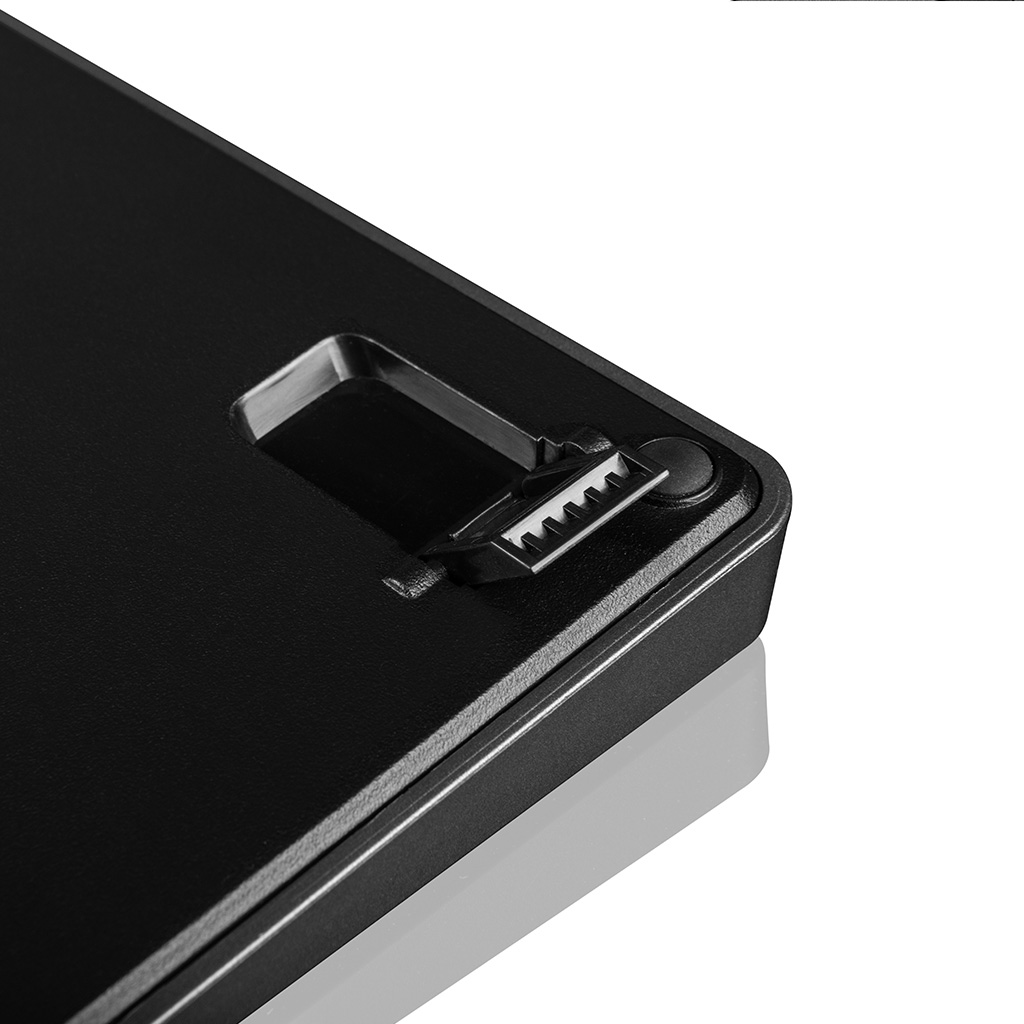 Zbliżenie czarnej, teksturowanej powierzchni z małą, ząbkowaną plastikową zatrzaską i okrągłym przyciskiem.