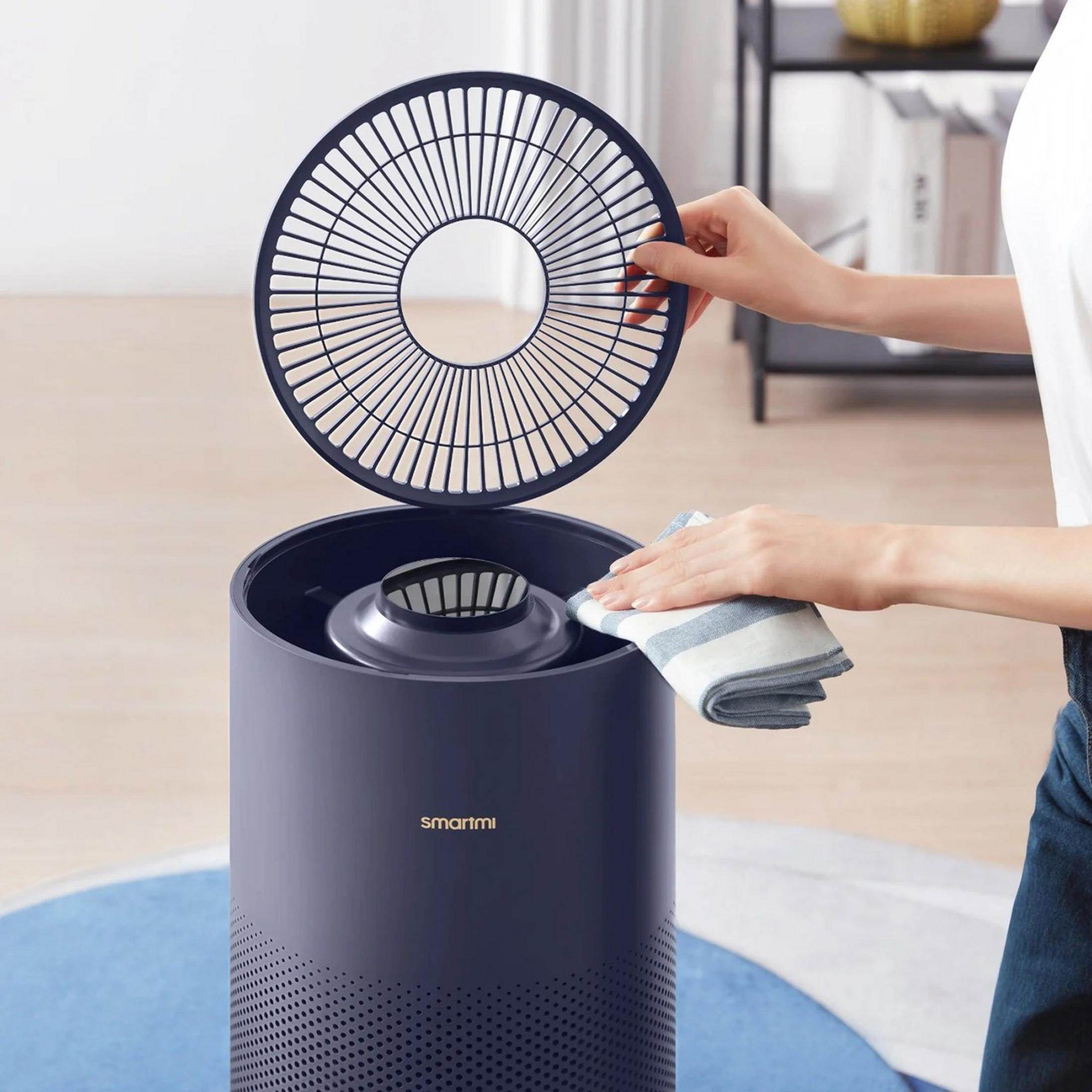 Persona pulisce un purificatore d'aria blu scuro con un panno a strisce.