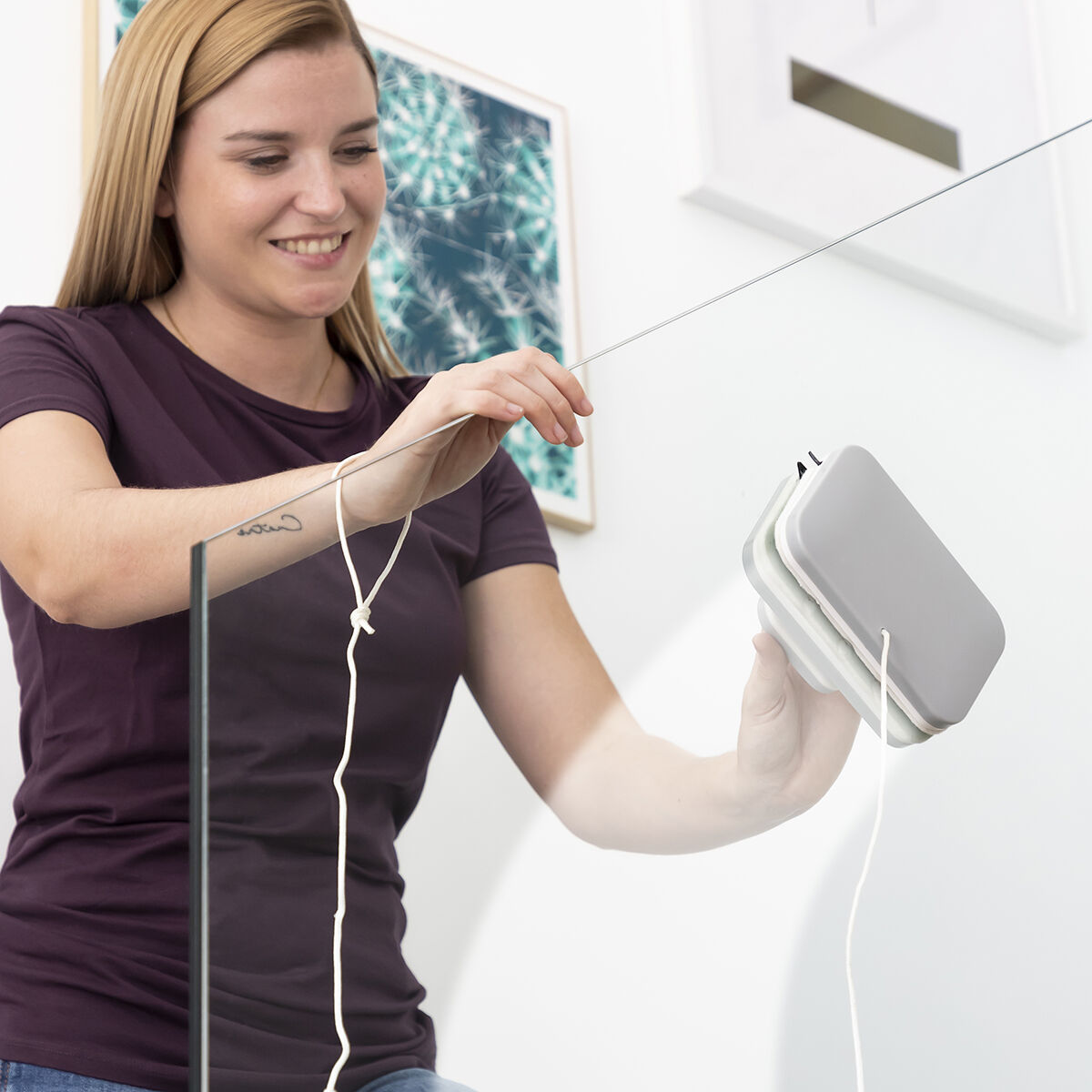 Mujer limpiando vidrio con limpiador magnético, sujetando una cuerda blanca.