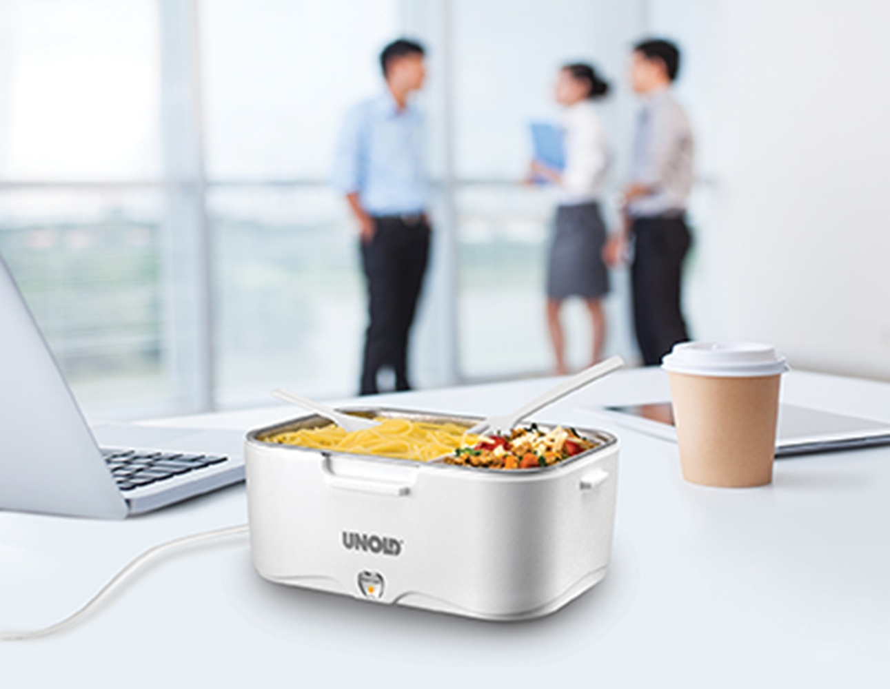 Eine weiße UNOLD-Brotbox mit Nudeln und Gemüse steht auf einem Schreibtisch neben einem Laptop und einem Kaffeebecher.