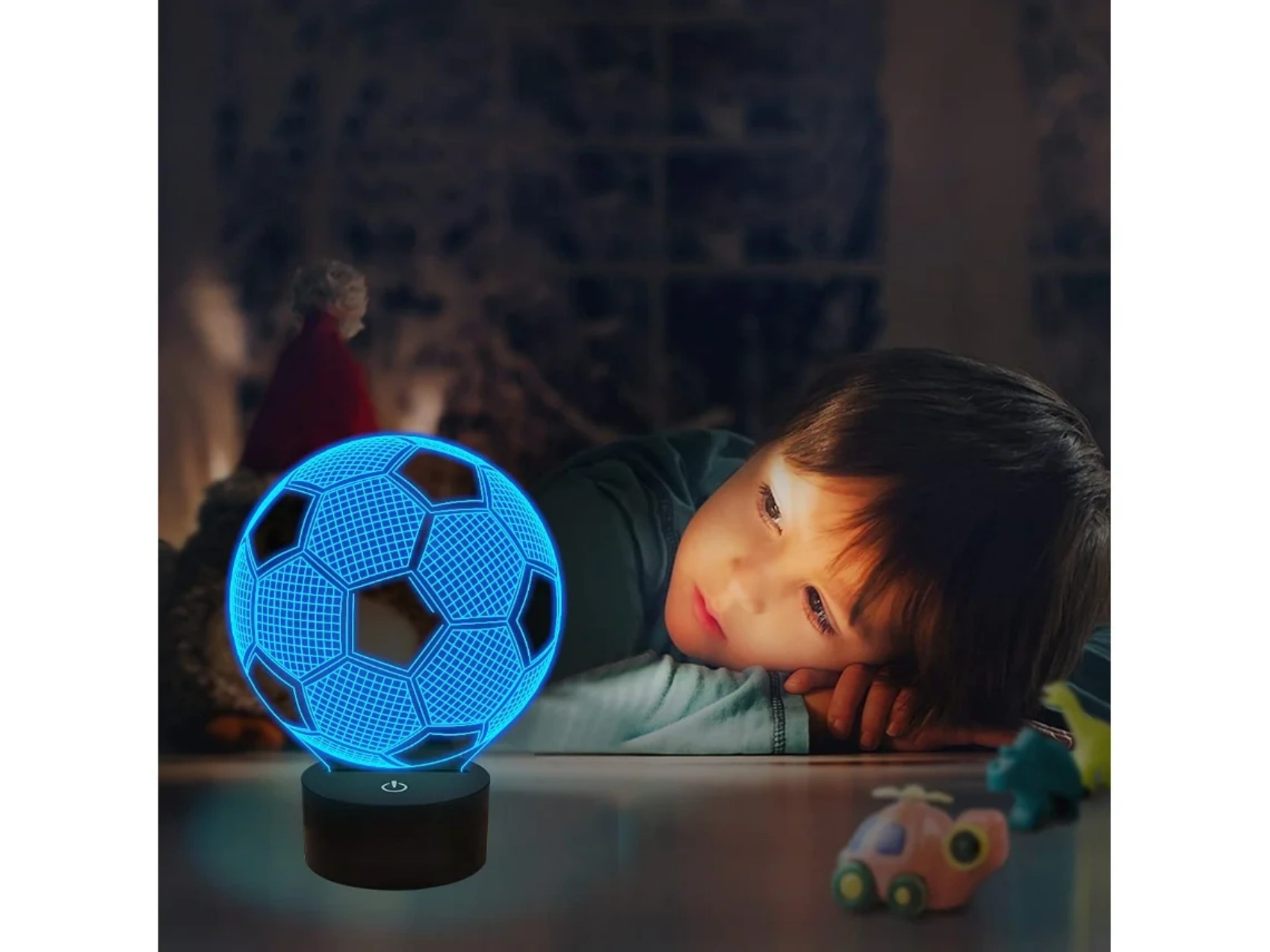 Junge schaut auf eine blaue Fußballlampe. Spielzeug auf dem Boden.
