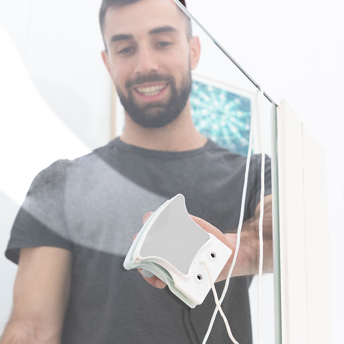 Hombre sonriendo, limpiando cristal con limpiador magnético. Limpiador blanco en cristal.