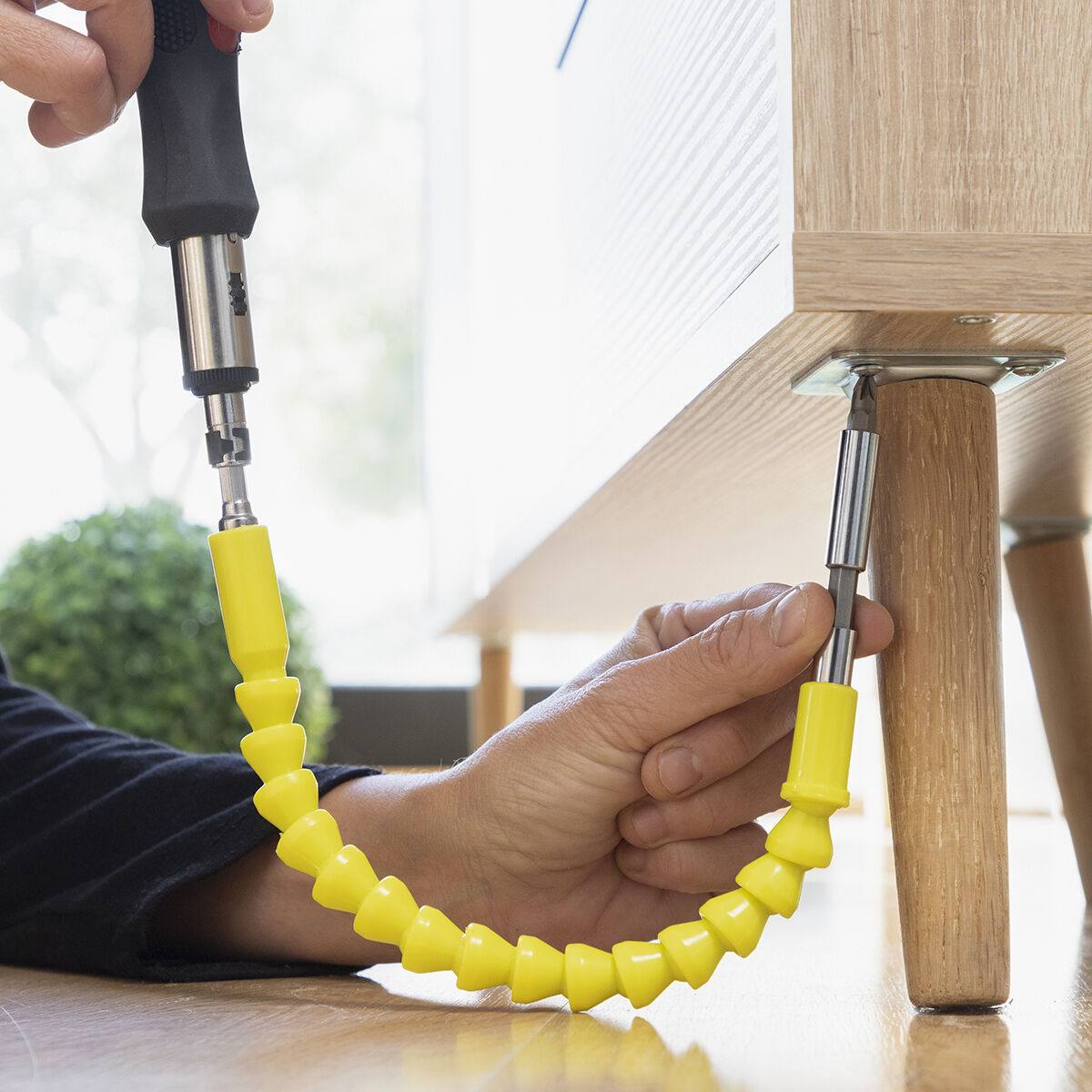 Mani usano una punta flessibile per avvitatore per fissare una gamba di legno a un pannello mobile.
