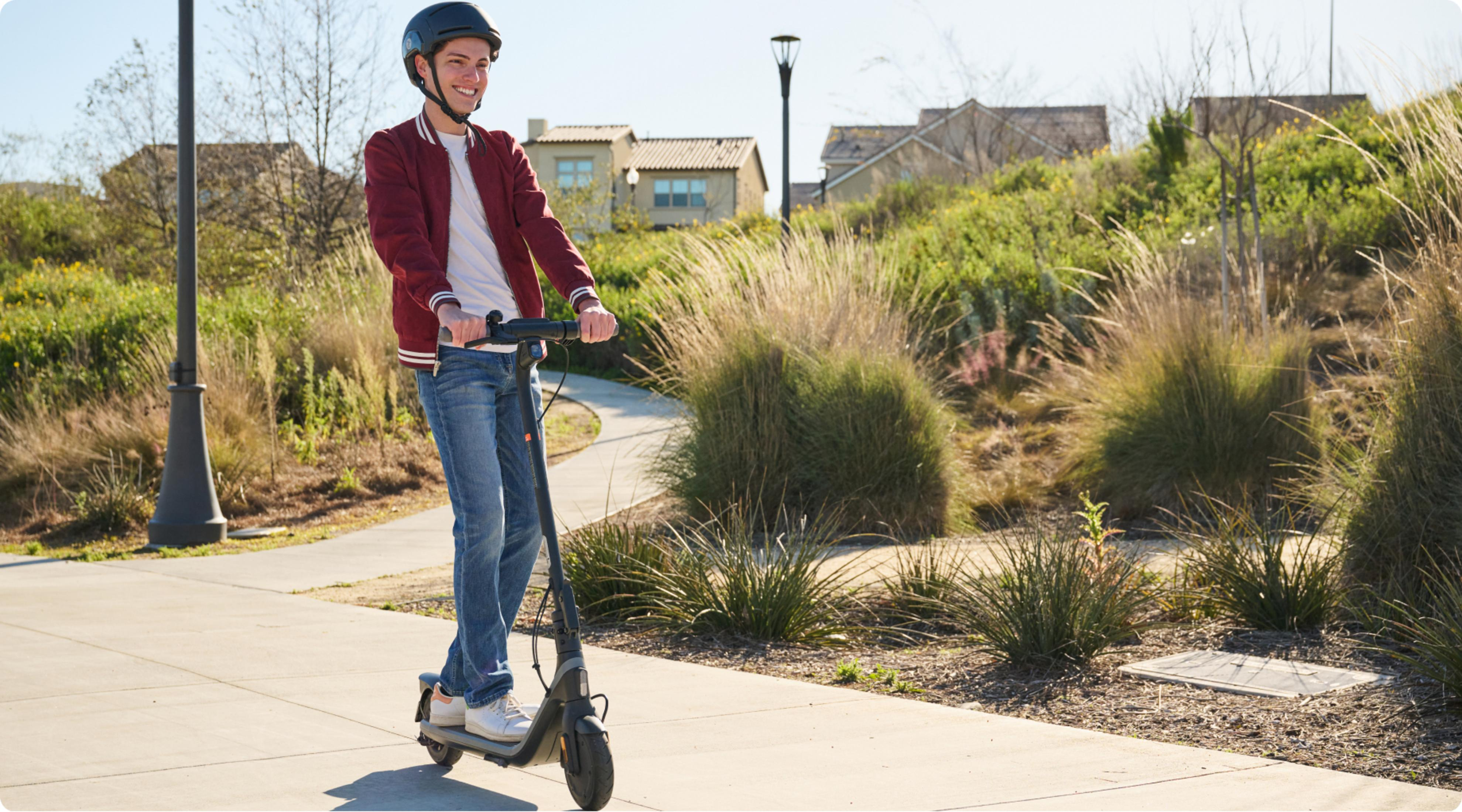 Adolescente sonriente con casco monta patinete eléctrico en sendero.