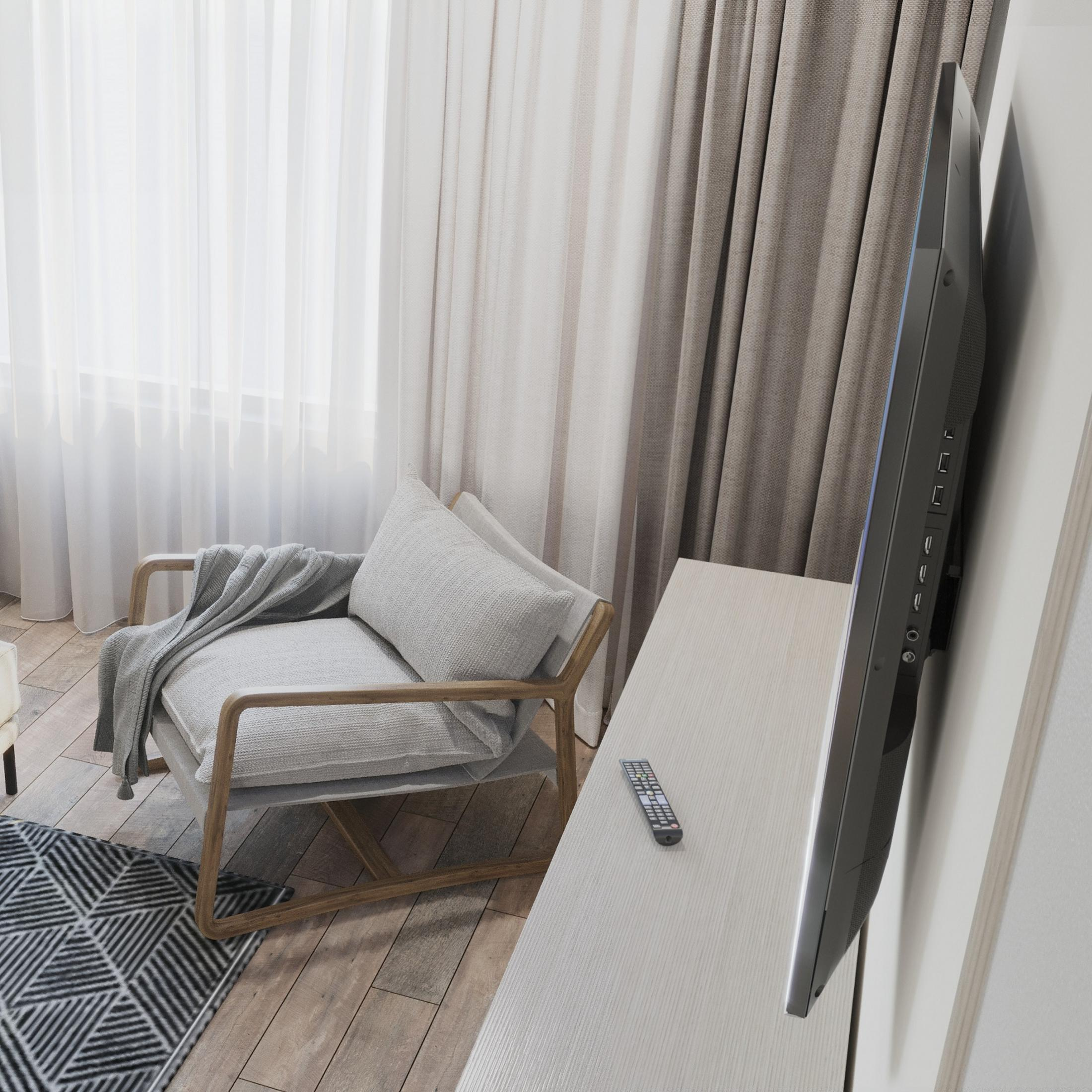 Una sala de estar moderna con sillón gris, cortinas transparentes y TV en la pared.