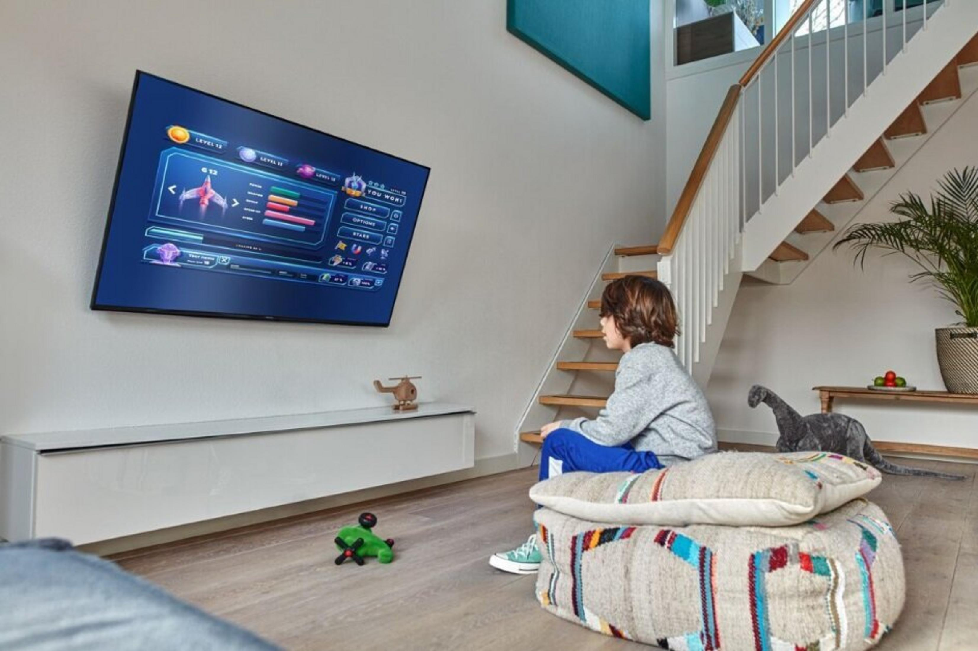 Chłopiec siedzi na poduszce podłogowej przed telewizorem wyświetlającym grę.