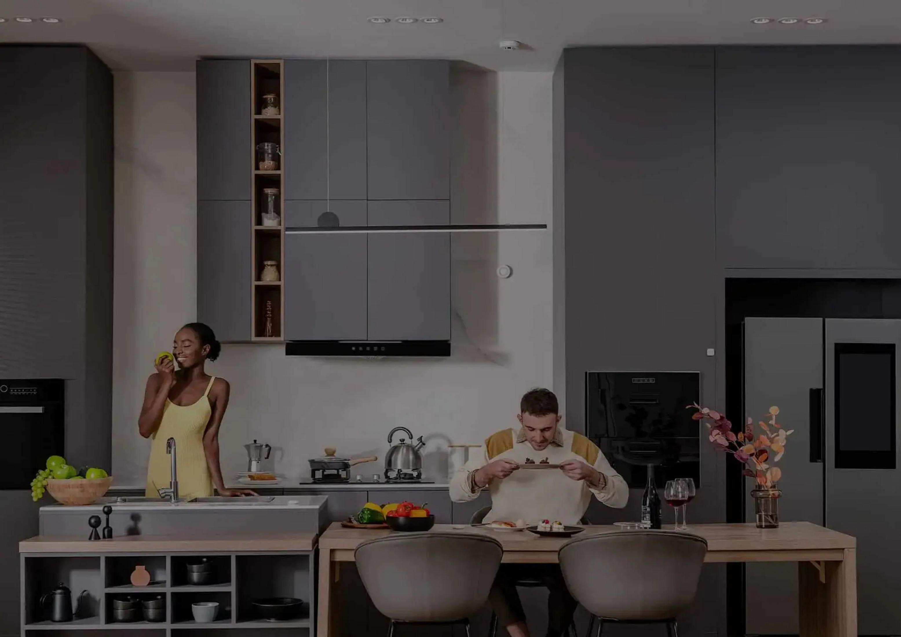 Kobieta w żółtym zjada jabłko w nowoczesnej kuchni. Mężczyzna je przy stole.