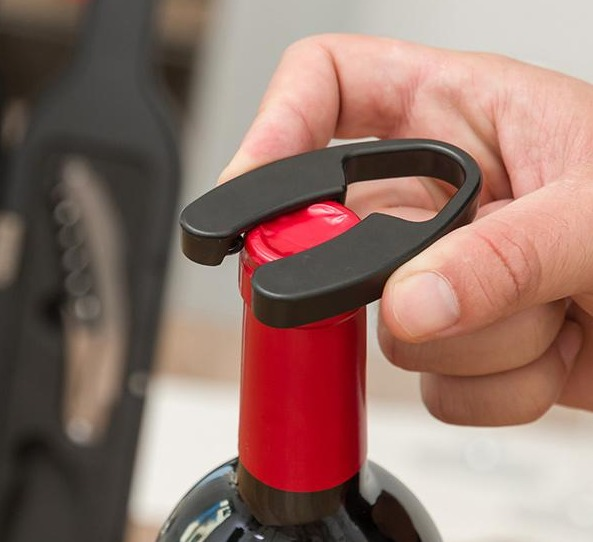 Una mano usa un sacacorchos negro para abrir una botella de vino con tapa roja.