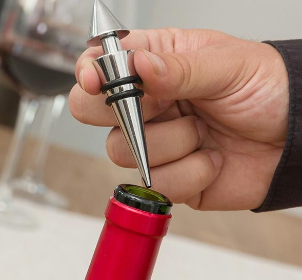 Una mano inserta un tapón de vino plateado en una botella de vino tinto.