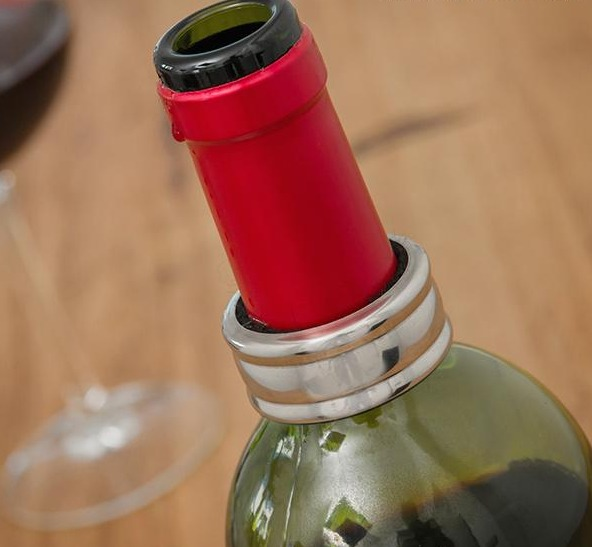 Primer plano de una botella de vino con sello rojo y anillo antigoteo plateado sobre fondo de madera.