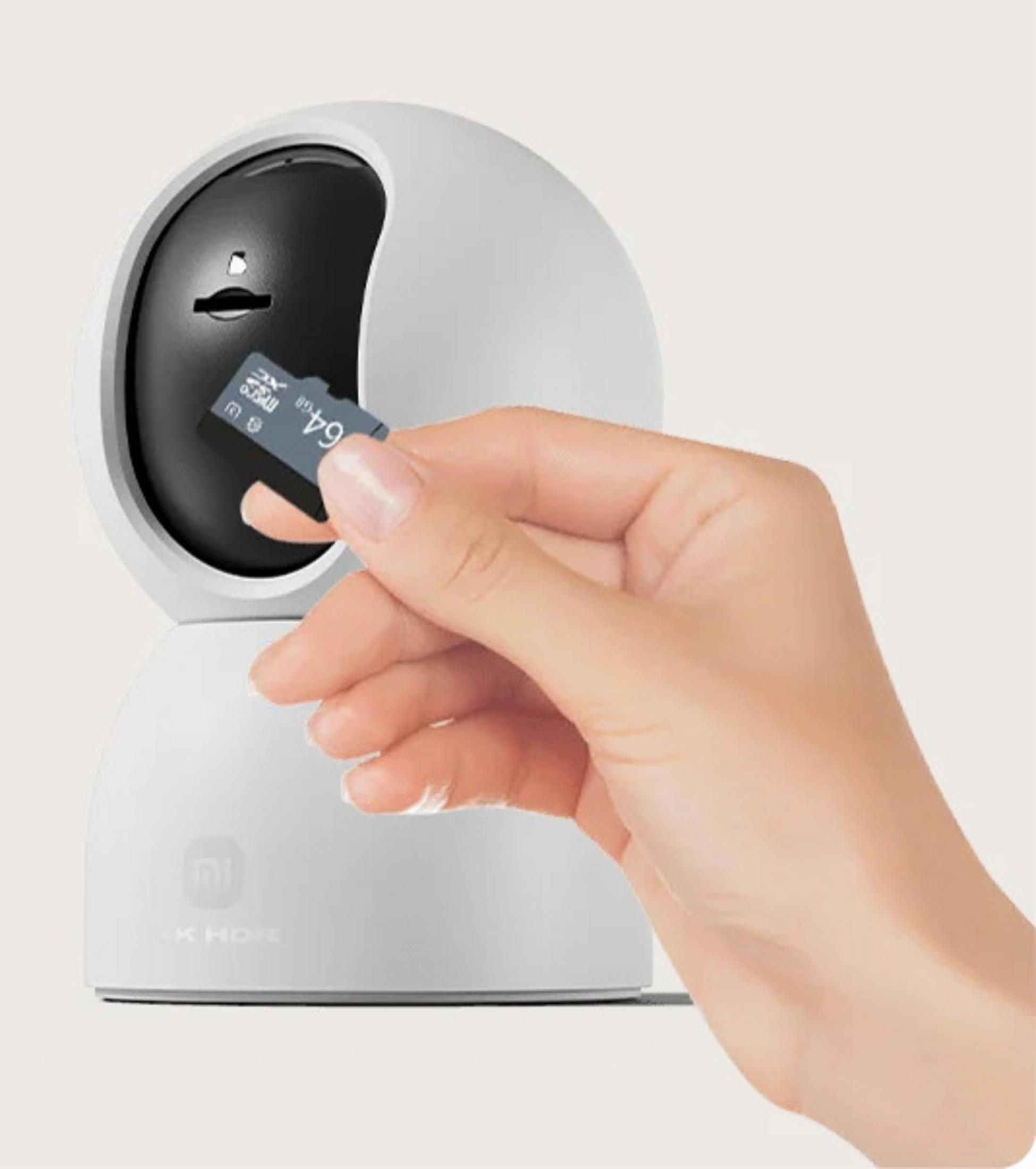 Ręka wkłada kartę microSD 64 GB do białej kamery bezpieczeństwa.