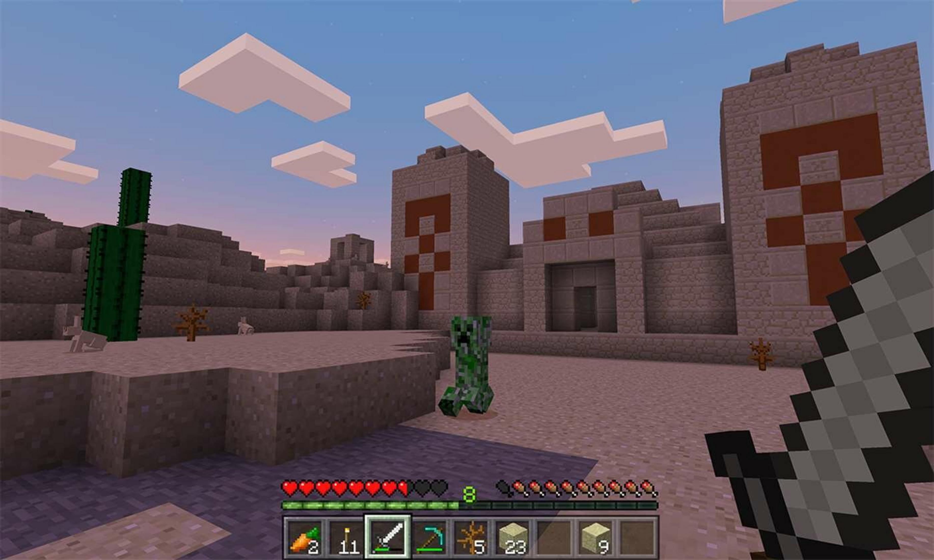 Una scena desertica di Minecraft con un creeper, cactus e strutture in pietra al tramonto.