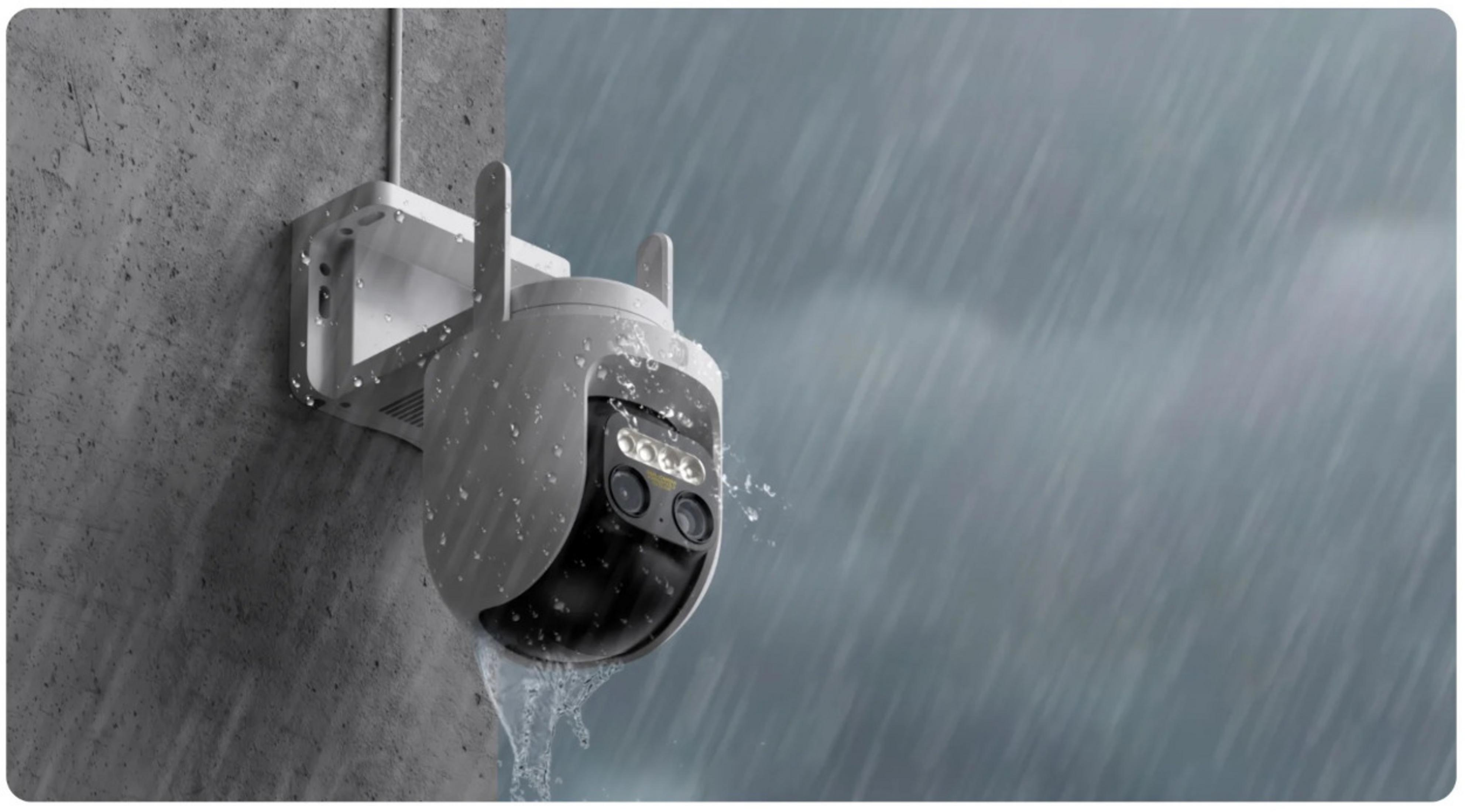 Biała kamera bezpieczeństwa zamontowana na szarej ścianie w ulewnym deszczu.