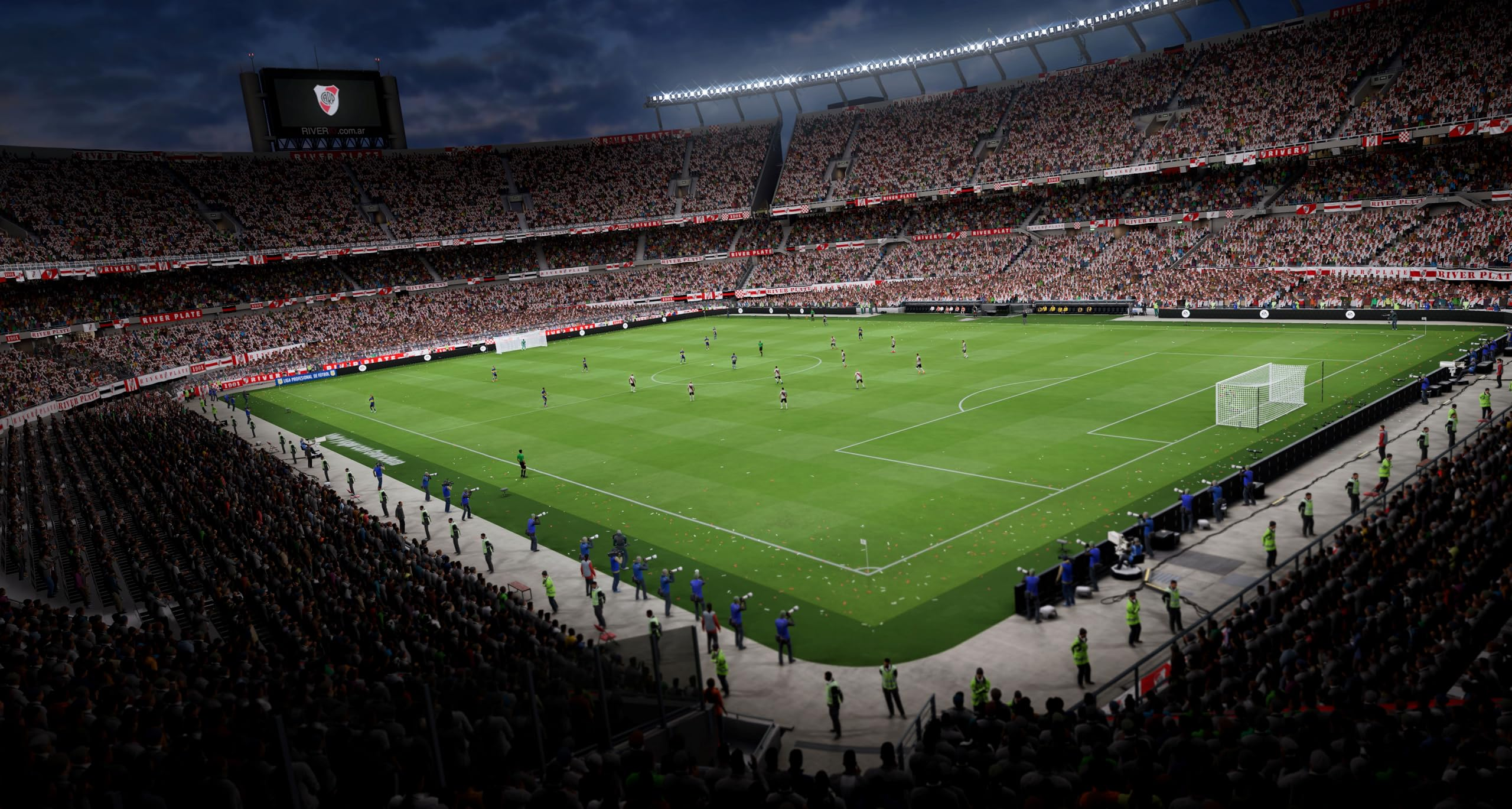 Uno stadio di calcio pieno di spettatori di notte, con giocatori sul campo verde.
