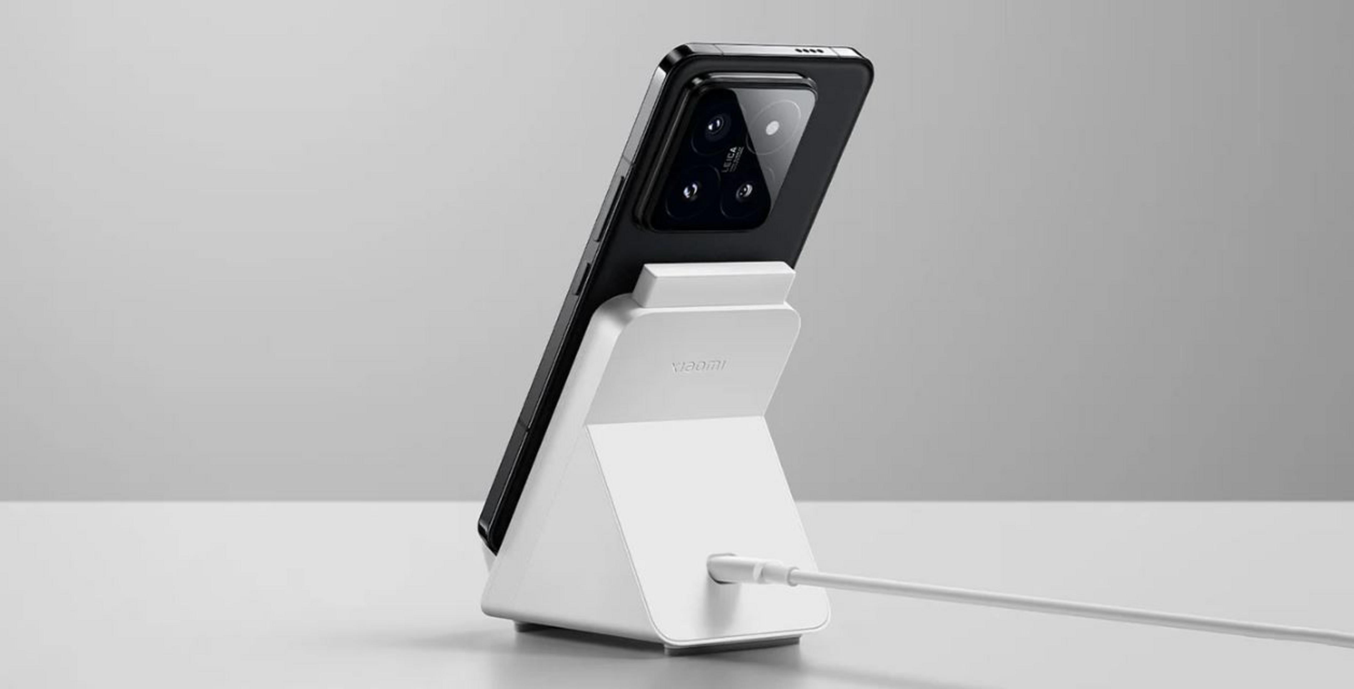 A black smartphone is charging on a white stand connected by a cable.
