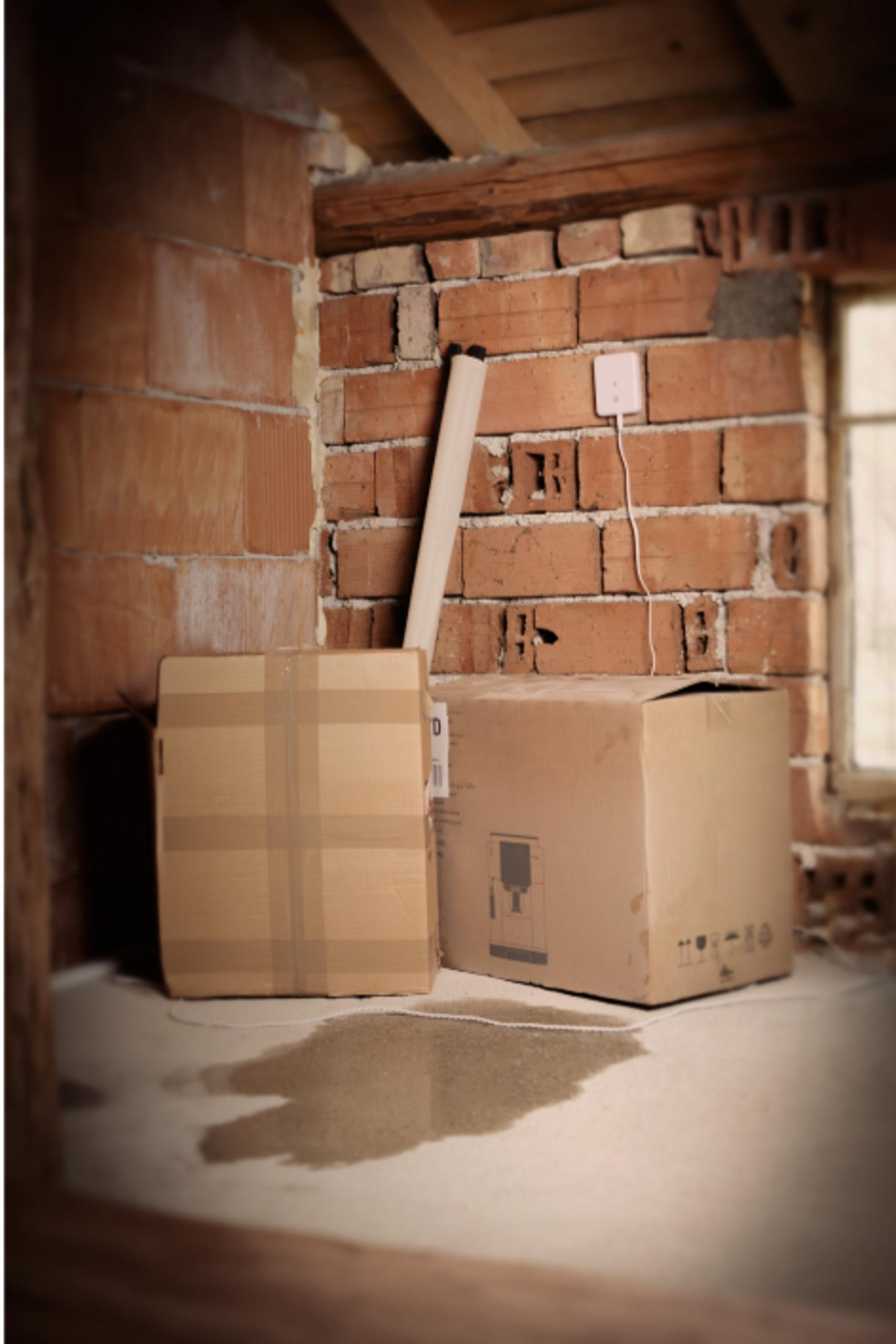 Dwa kartony stoją na mokrej podłodze obok ceglanego muru.