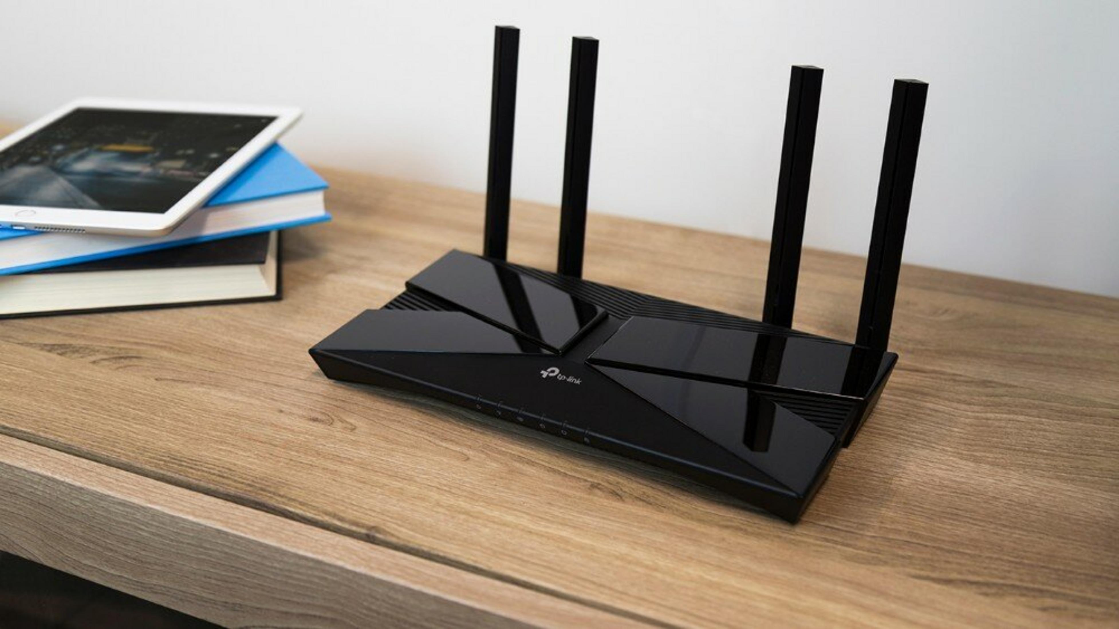 Czarny router Wi-Fi TP-Link z czterema antenami stoi na drewnianym biurku obok stosu książek i tabletu.