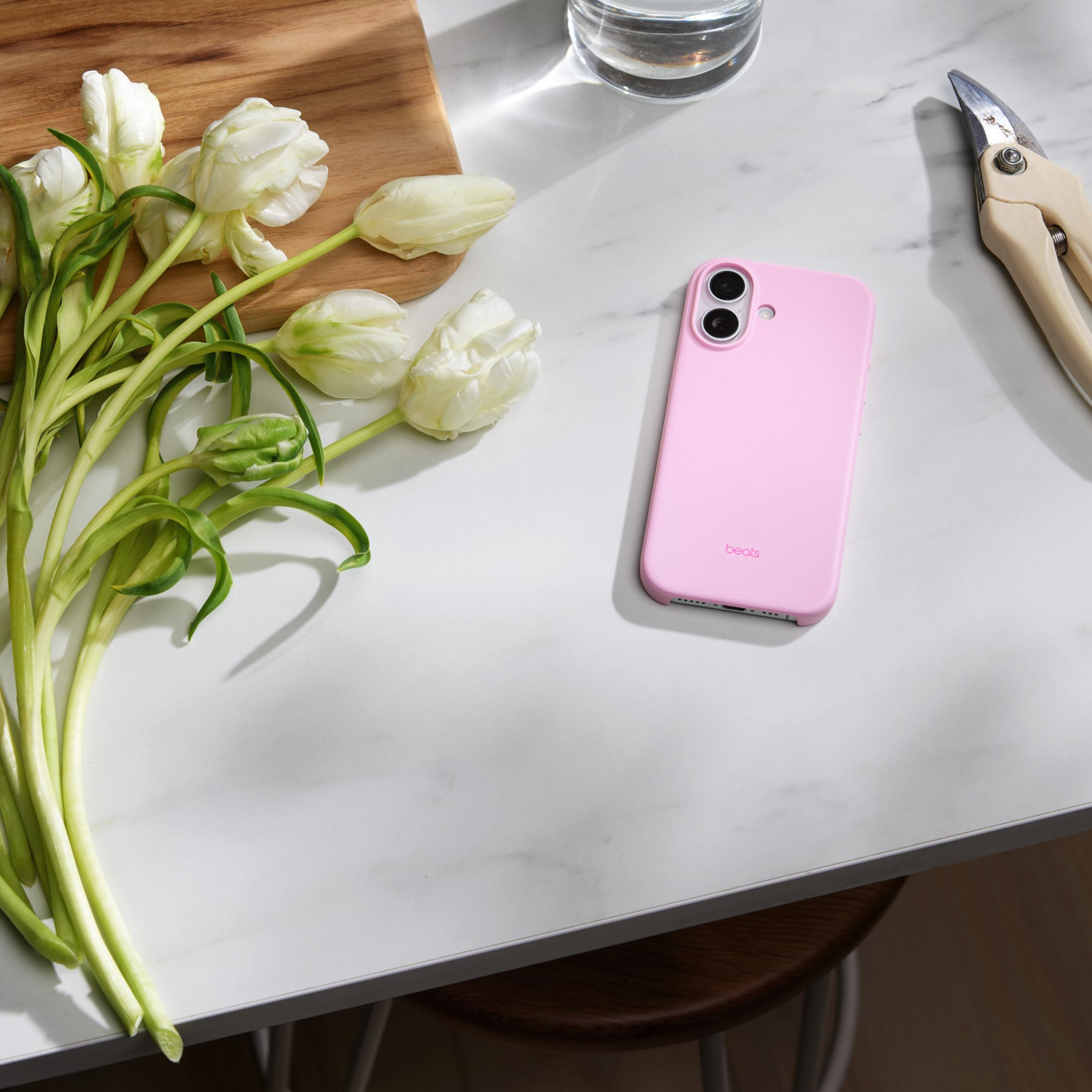 Ein rosafarbenes Smartphone liegt neben weißen Tulpen und einer Gartenschere.
