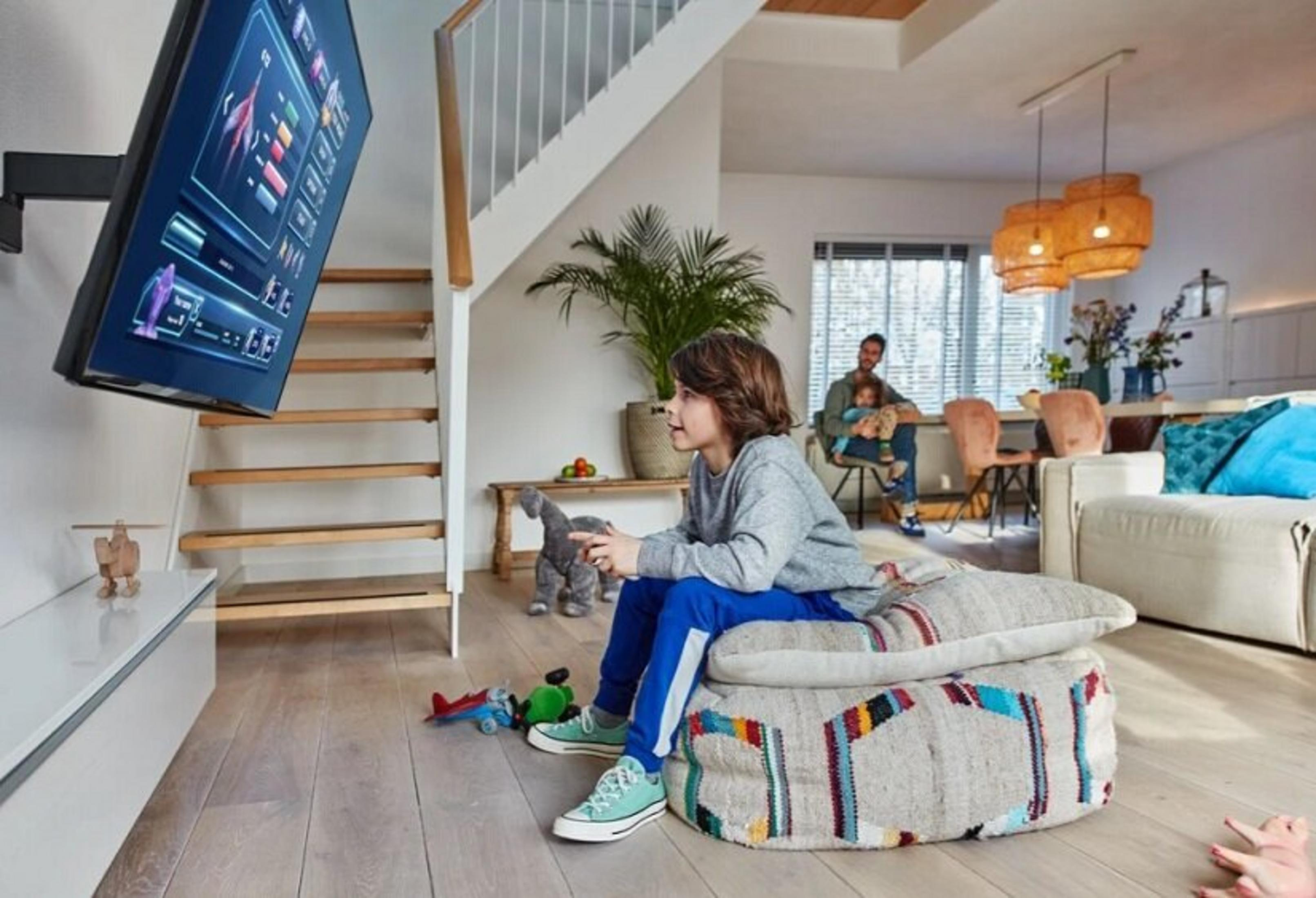 Un niño juega videojuegos en una sala de estar, con una familia al fondo.