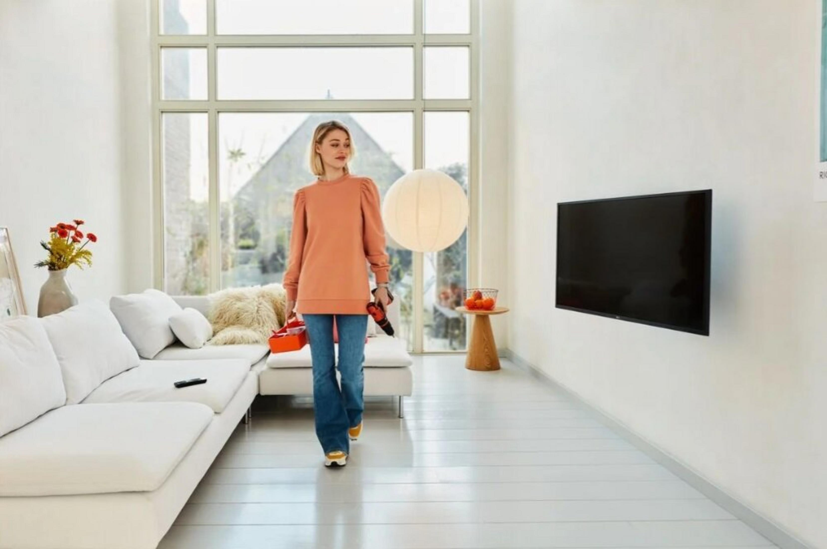 Kobieta przechodzi przez jasny salon z pudełkiem na narzędzia i wiertarką.